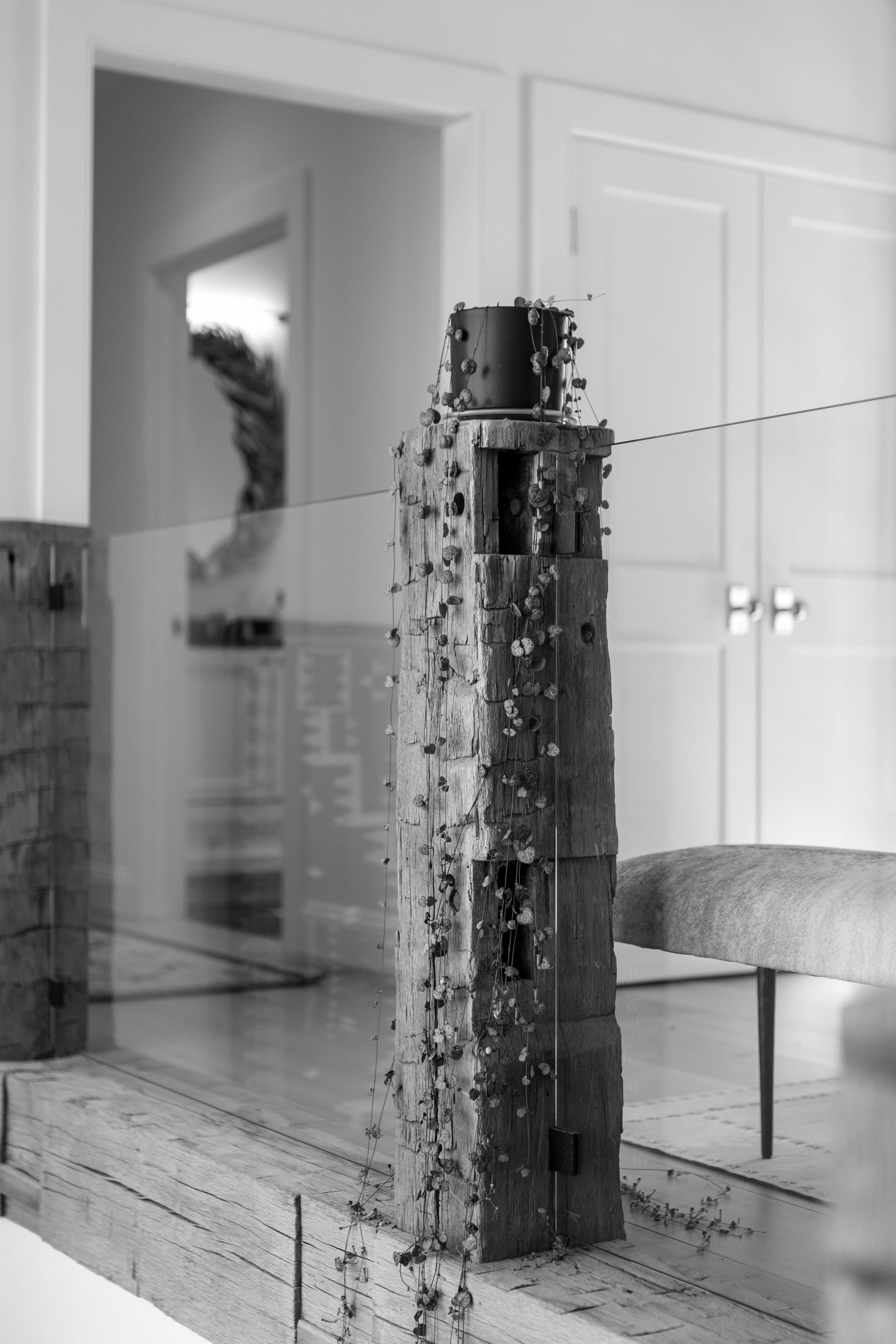 A tall, textured, stone-like sculpture sits on a ledge in a bright, modern room, partially reflected in a glass panel.