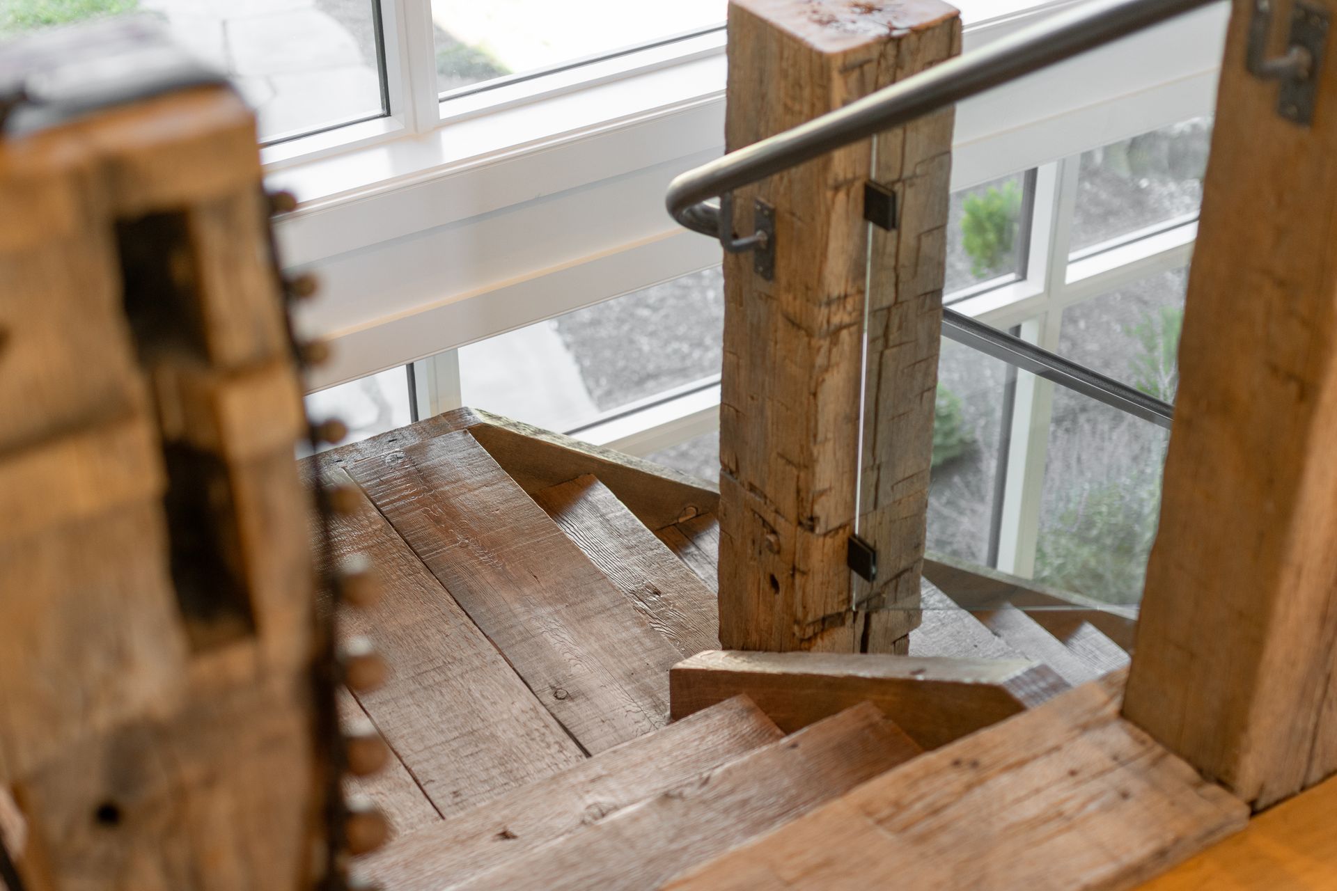A top-down view of rustic wooden stairs with heavy timber newel posts and a metal handrail, bathed in natural light.