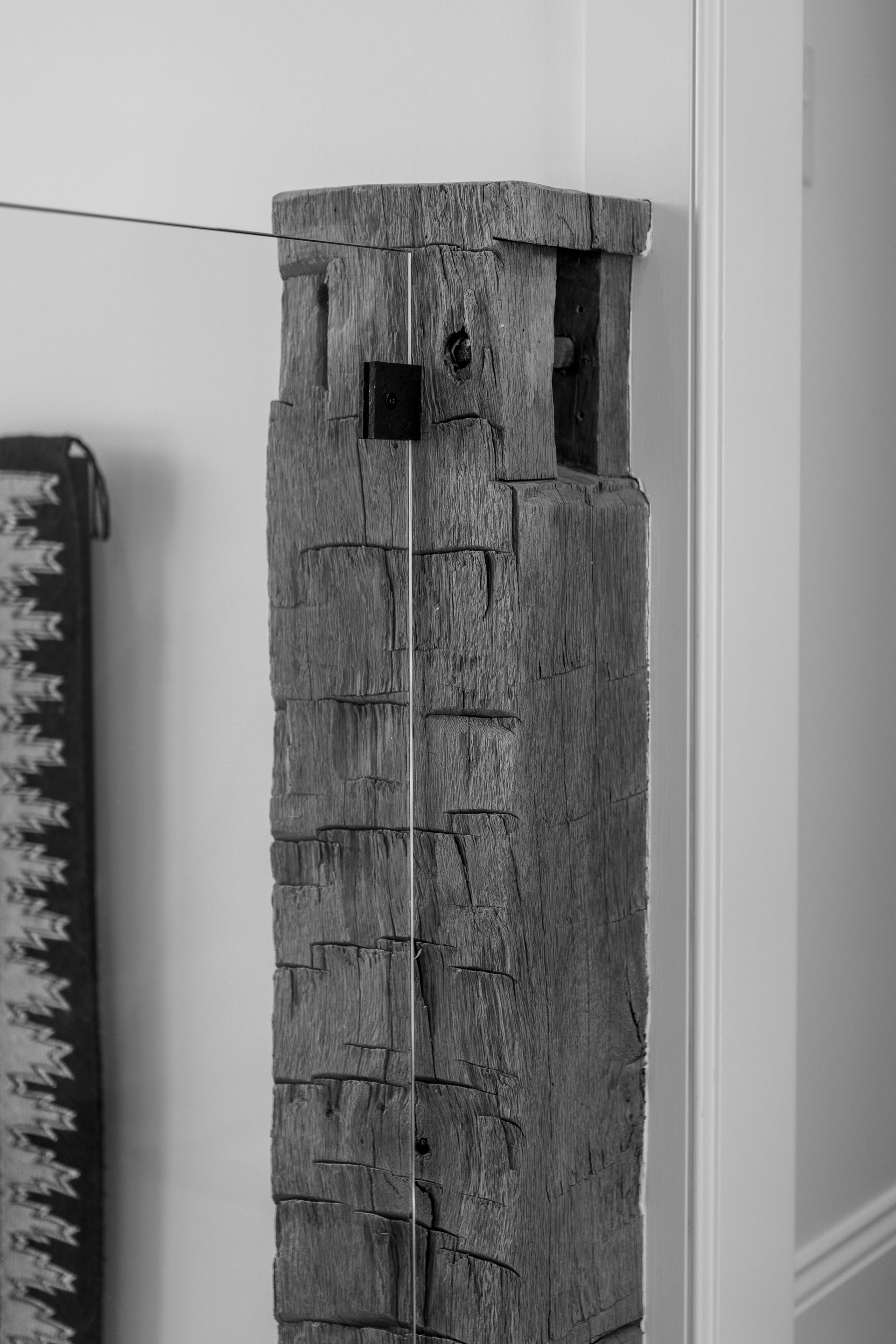 A rustic, weathered wood post stands vertically against a white wall with a black sensor attached near the top.