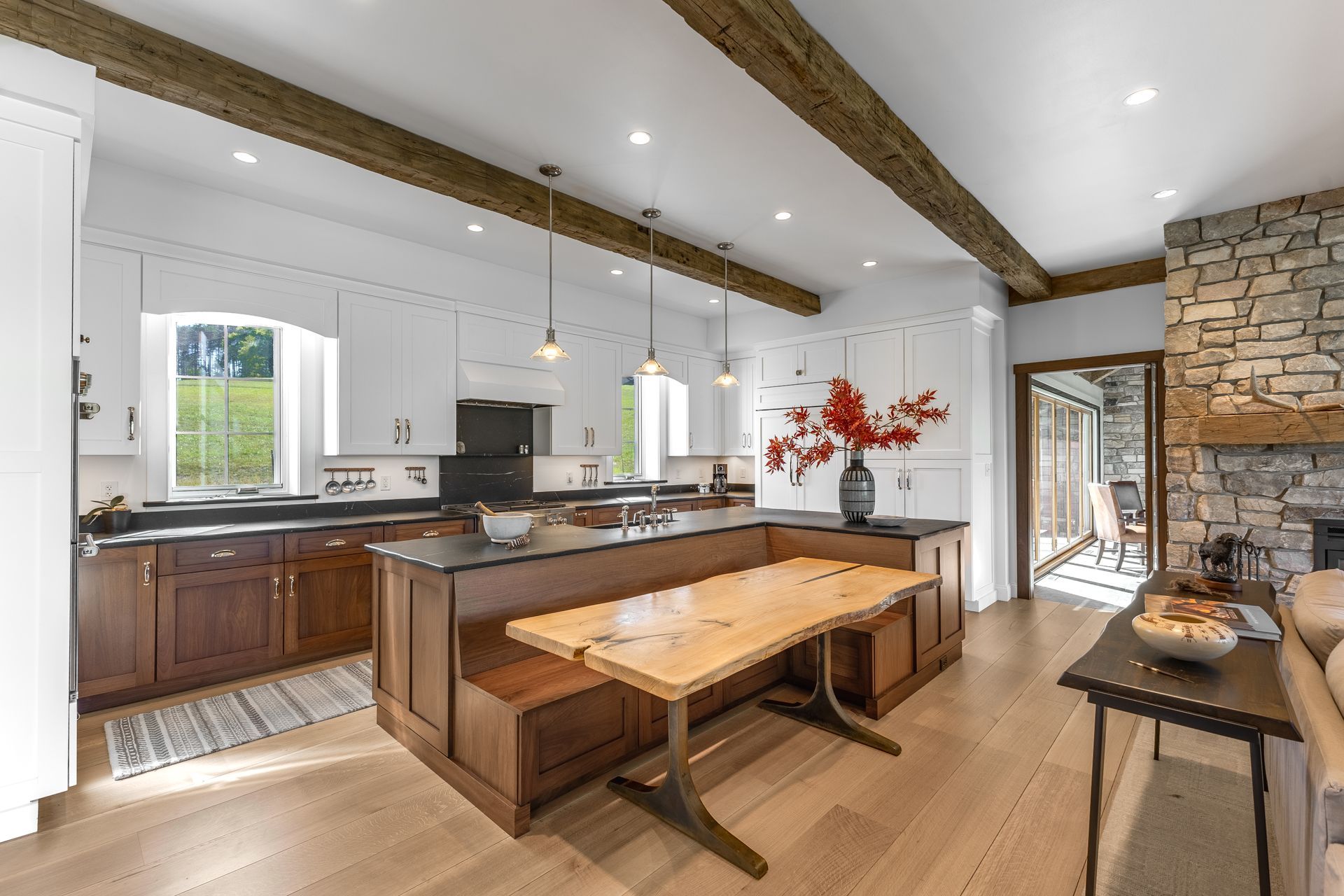 A rustic-modern kitchen with white upper cabinets, brown lower cabinets, a wood island table, and a stone fireplace.