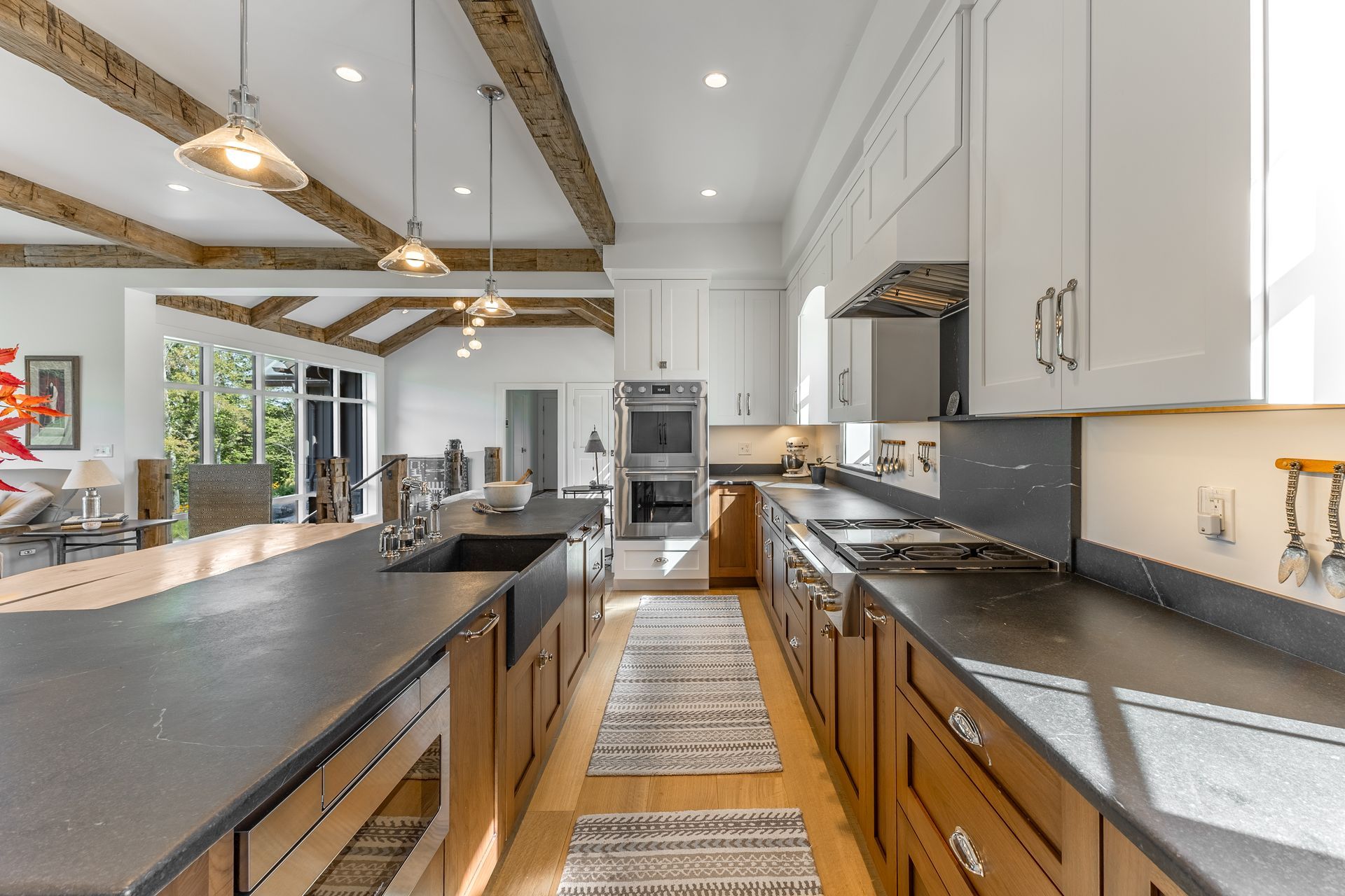 Modern kitchen with wooden lower cabinets, white upper cabinets, dark countertops, and exposed ceiling beams.
