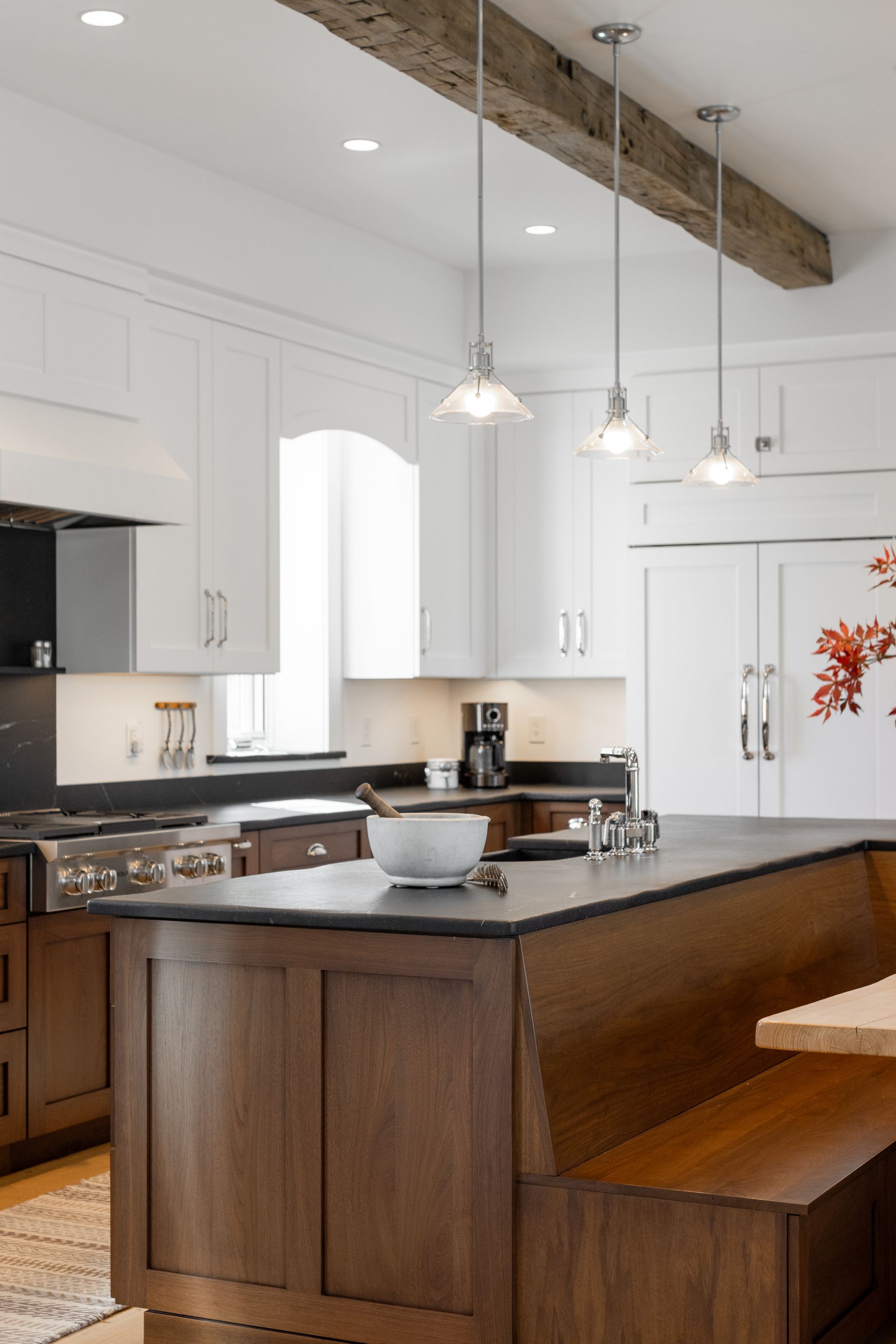 A modern kitchen featuring white cabinets, dark countertops, a wooden island with built-in seating, and three pendants.
