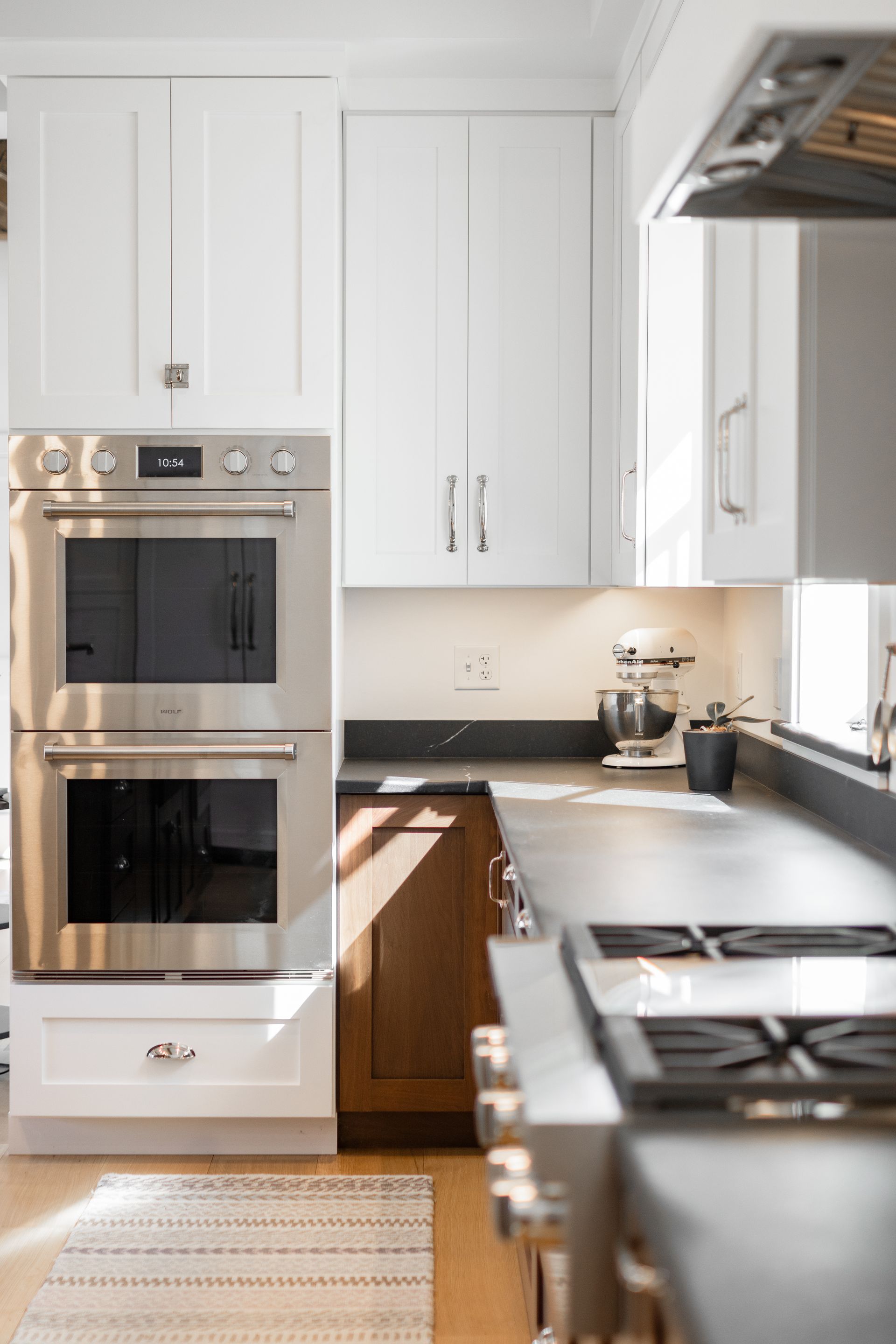 A modern kitchen featuring white upper cabinets, a stainless steel wall oven, dark countertops, and a stovetop.
