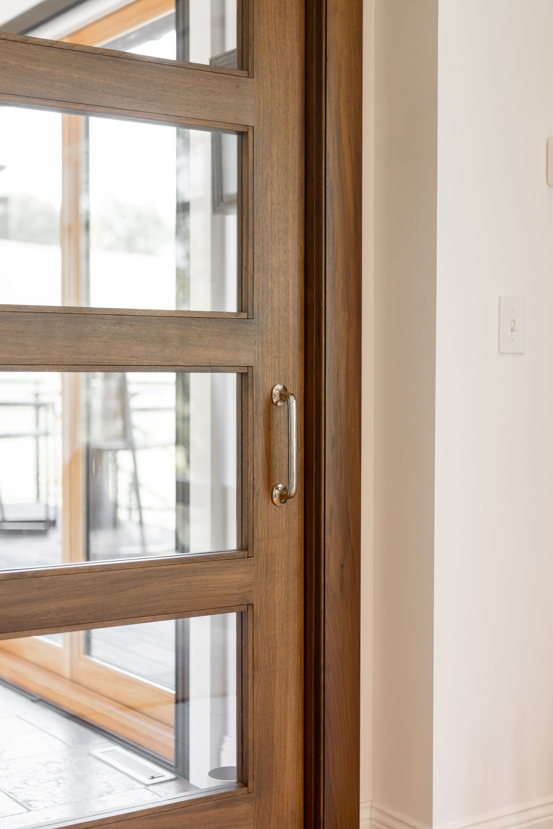 A close-up of a rustic wooden door with glass panels and a metallic handle, positioned next to a white interior wall.
