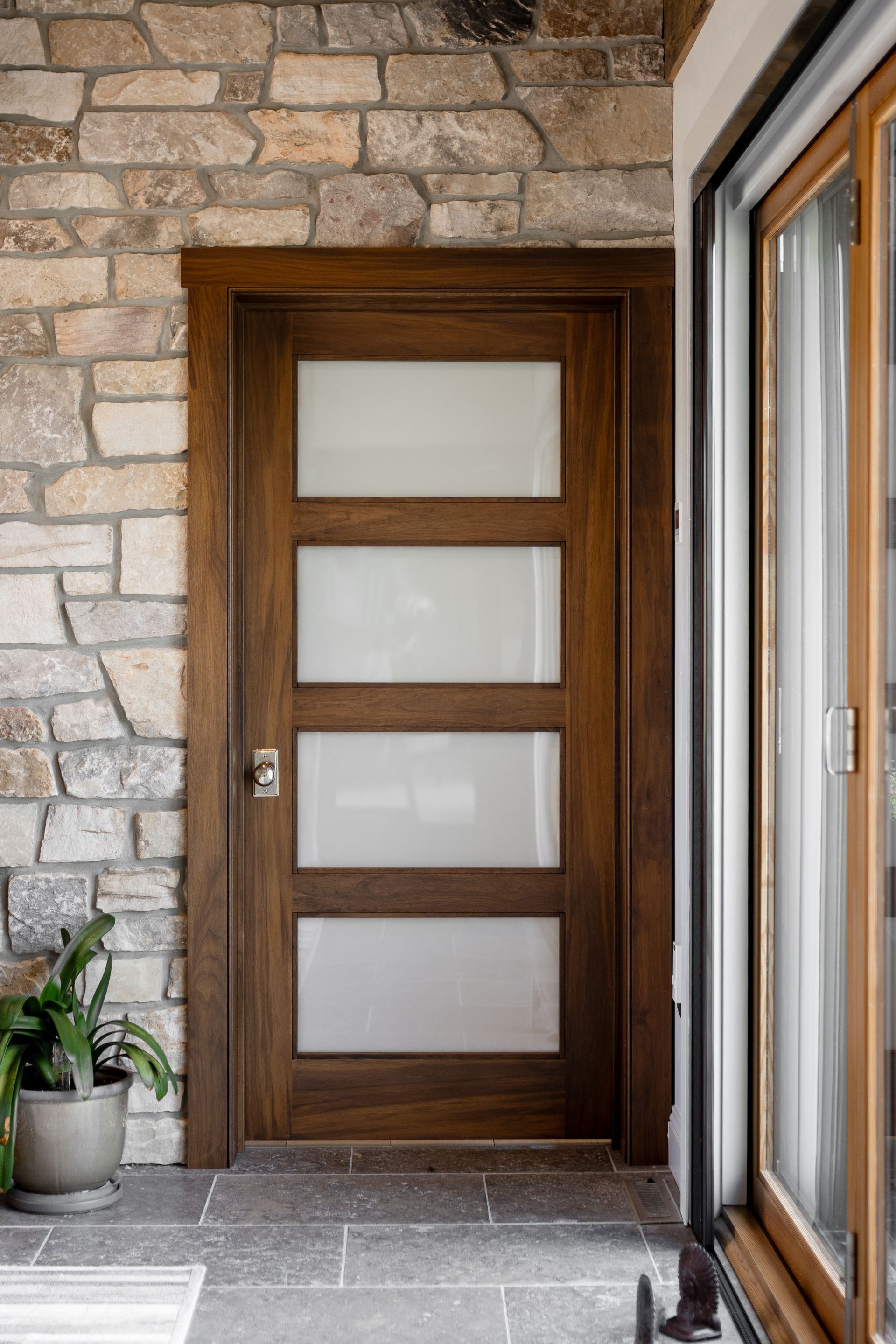 A wood door with four horizontal frosted glass panels set into a stone wall next to a large window.