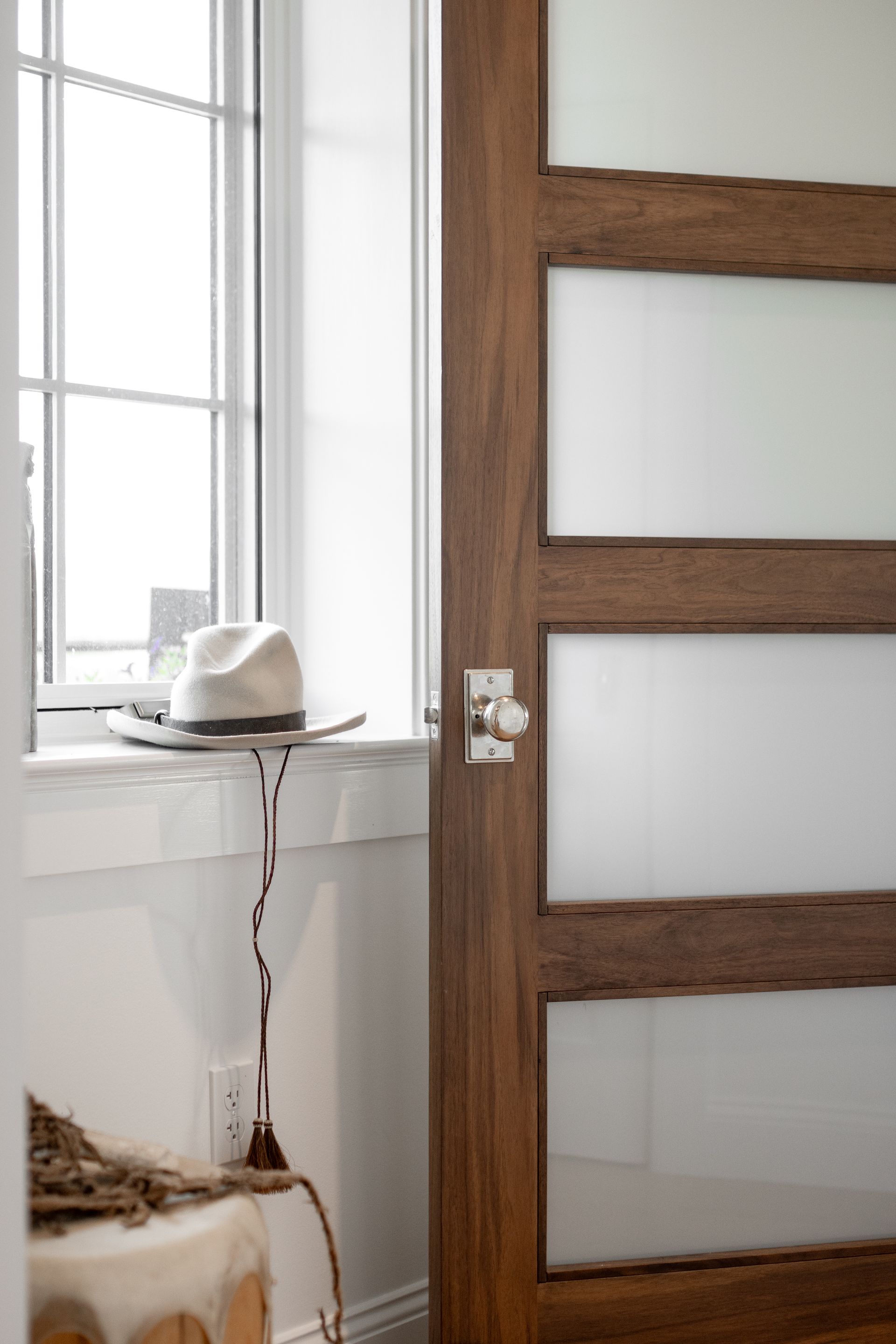 A fedora sits on a windowsill next to a dark wood door with frosted glass panels.