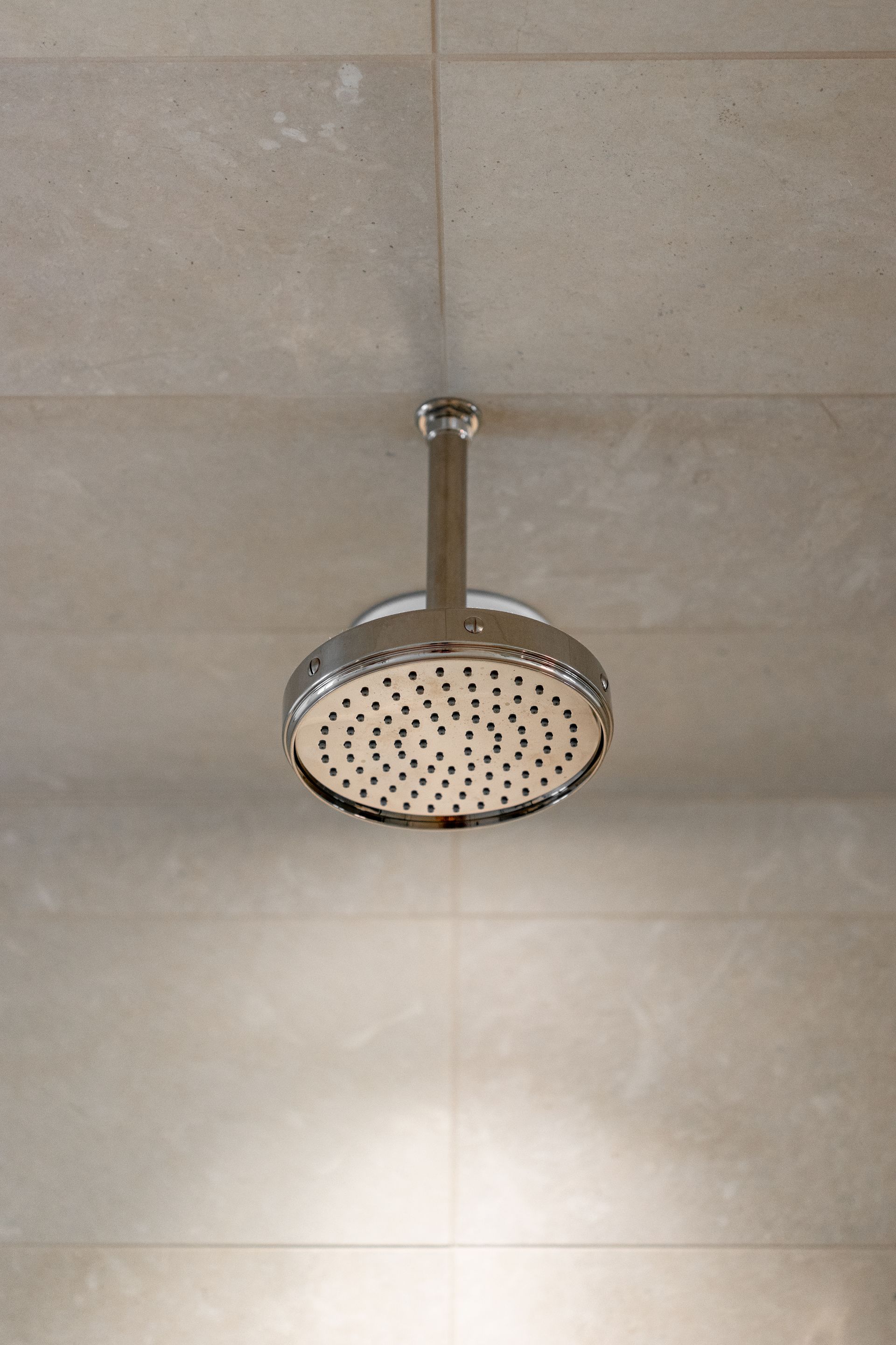 A modern circular chrome shower head mounted on a tiled ceiling.