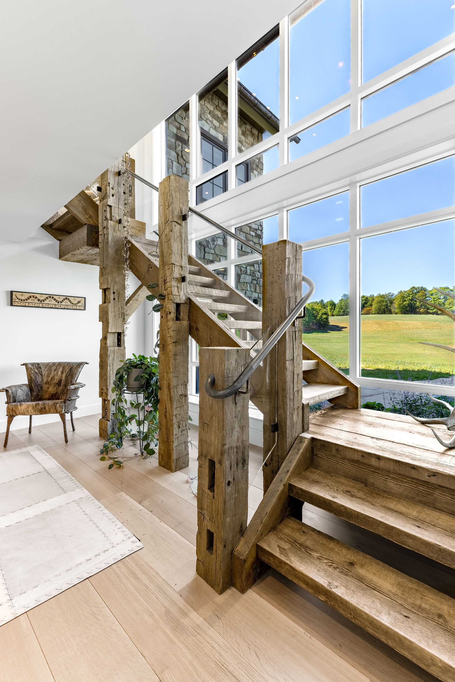 Rustic stairway with large windows overlooking a bright green landscape.