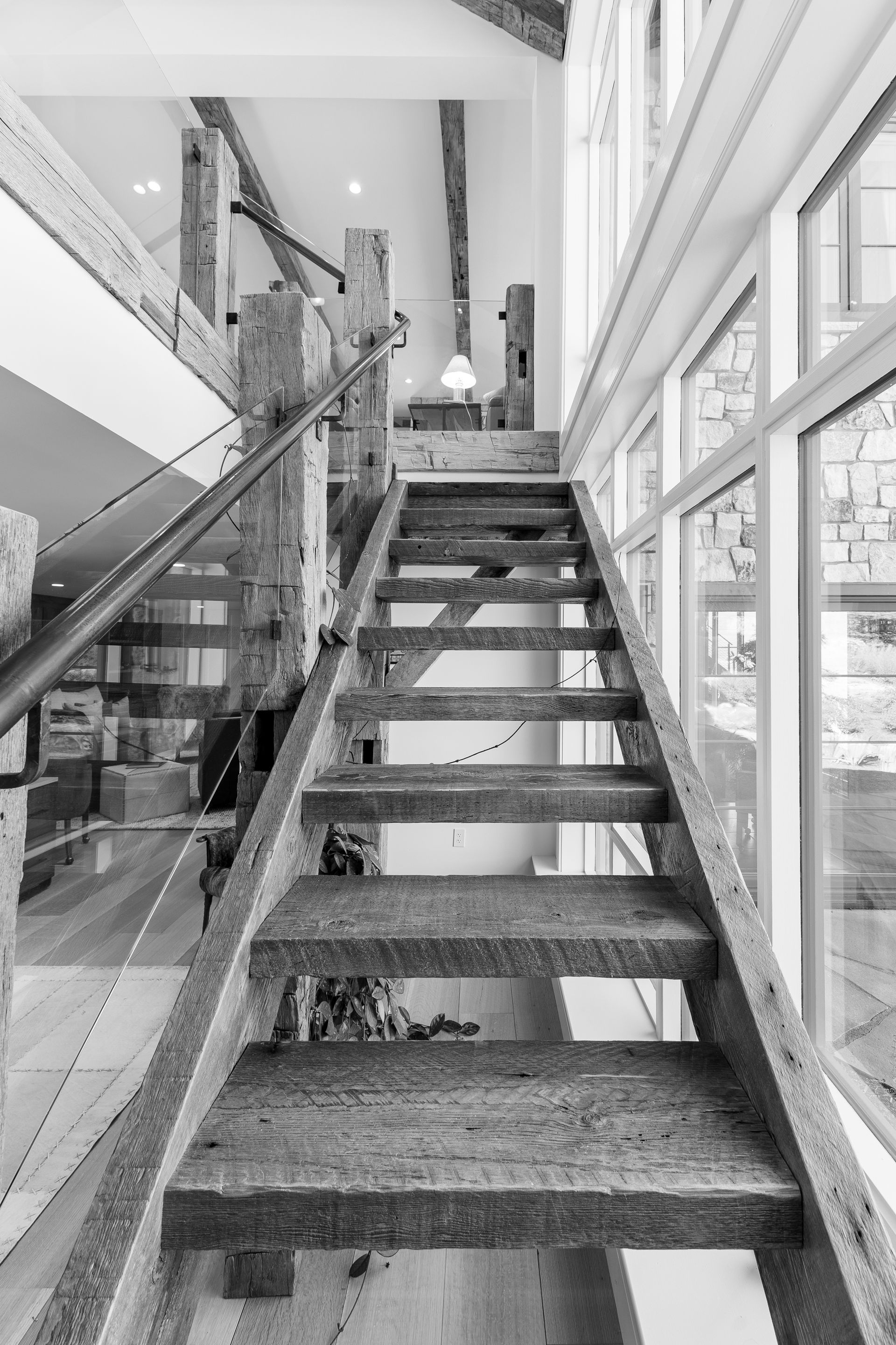 Wooden staircase in a bright modern interior with large windows and glass railing.