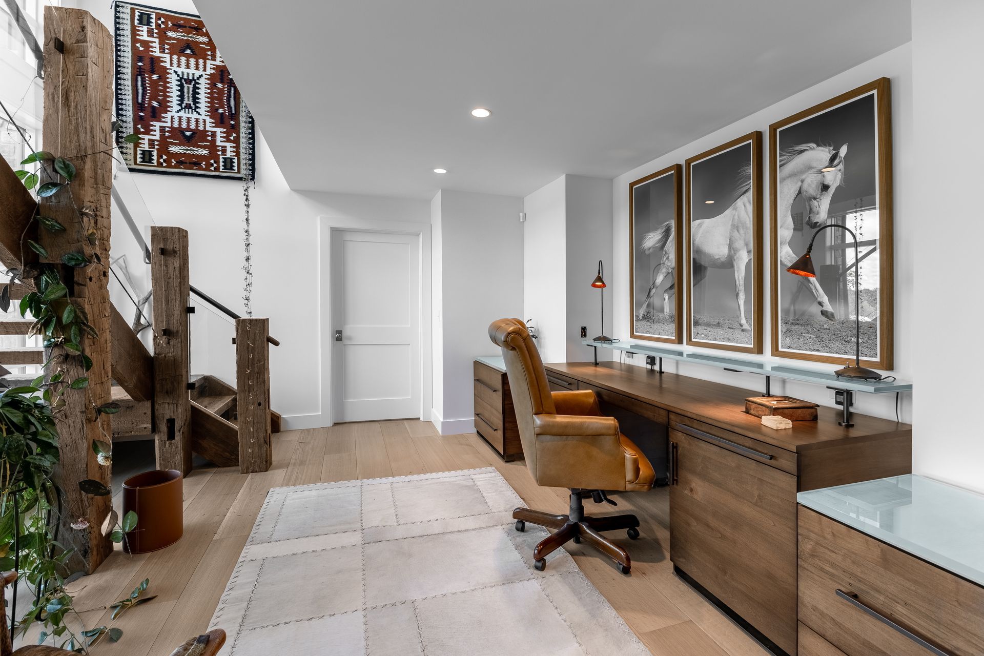 Modern home office with desk, chair, mirror, and staircase in a bright hallway