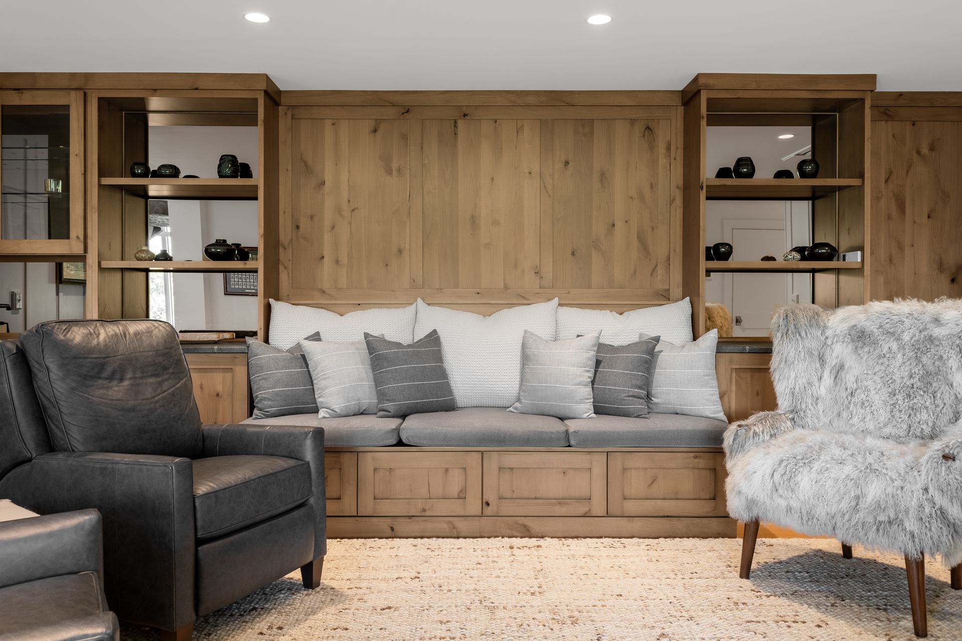 Cozy living room with built-in wood shelving, a bench seat, and two armchairs by the fireplace wall