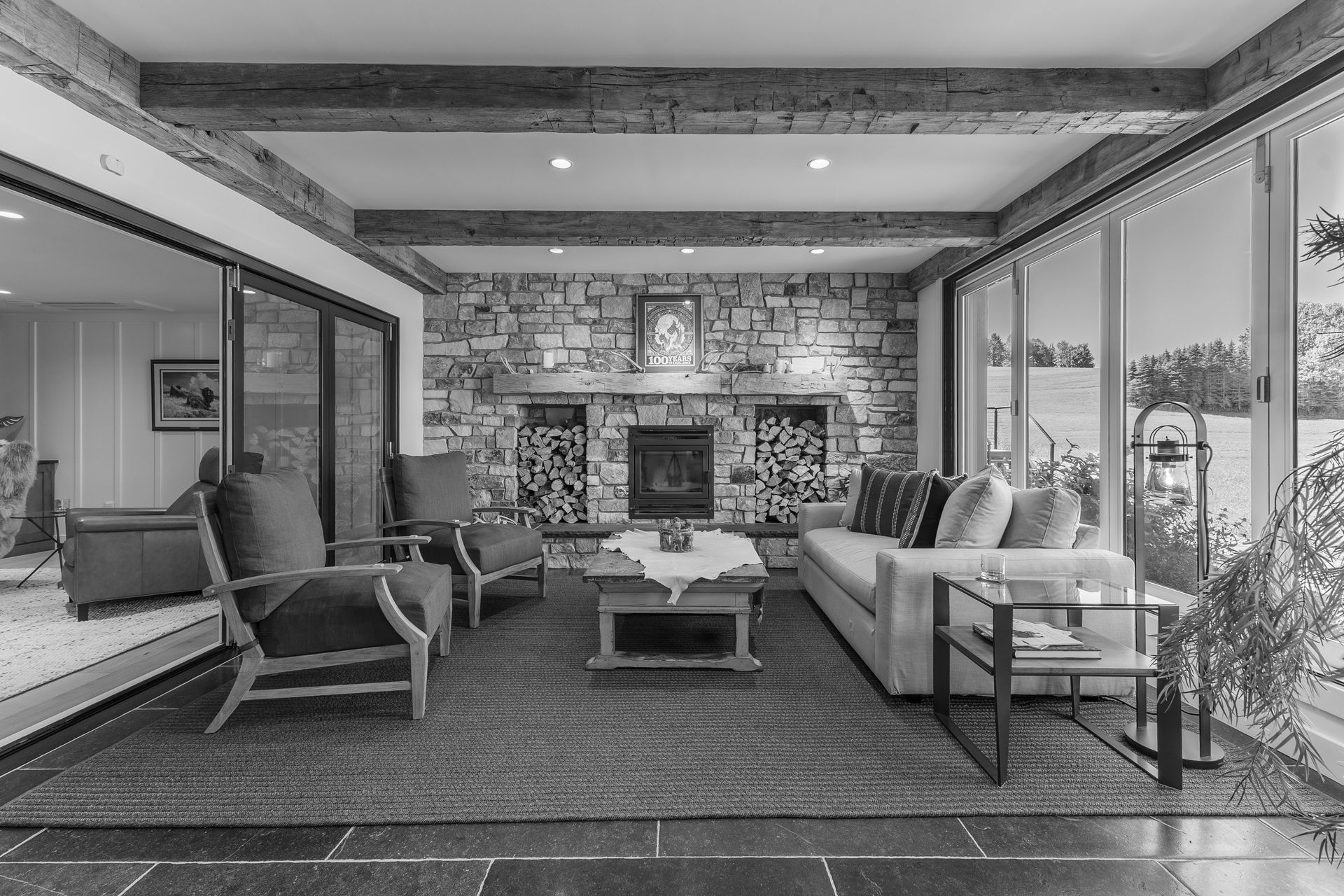 Modern living room with stone fireplace, sofas, chairs, coffee table, and large windows overlooking a patio