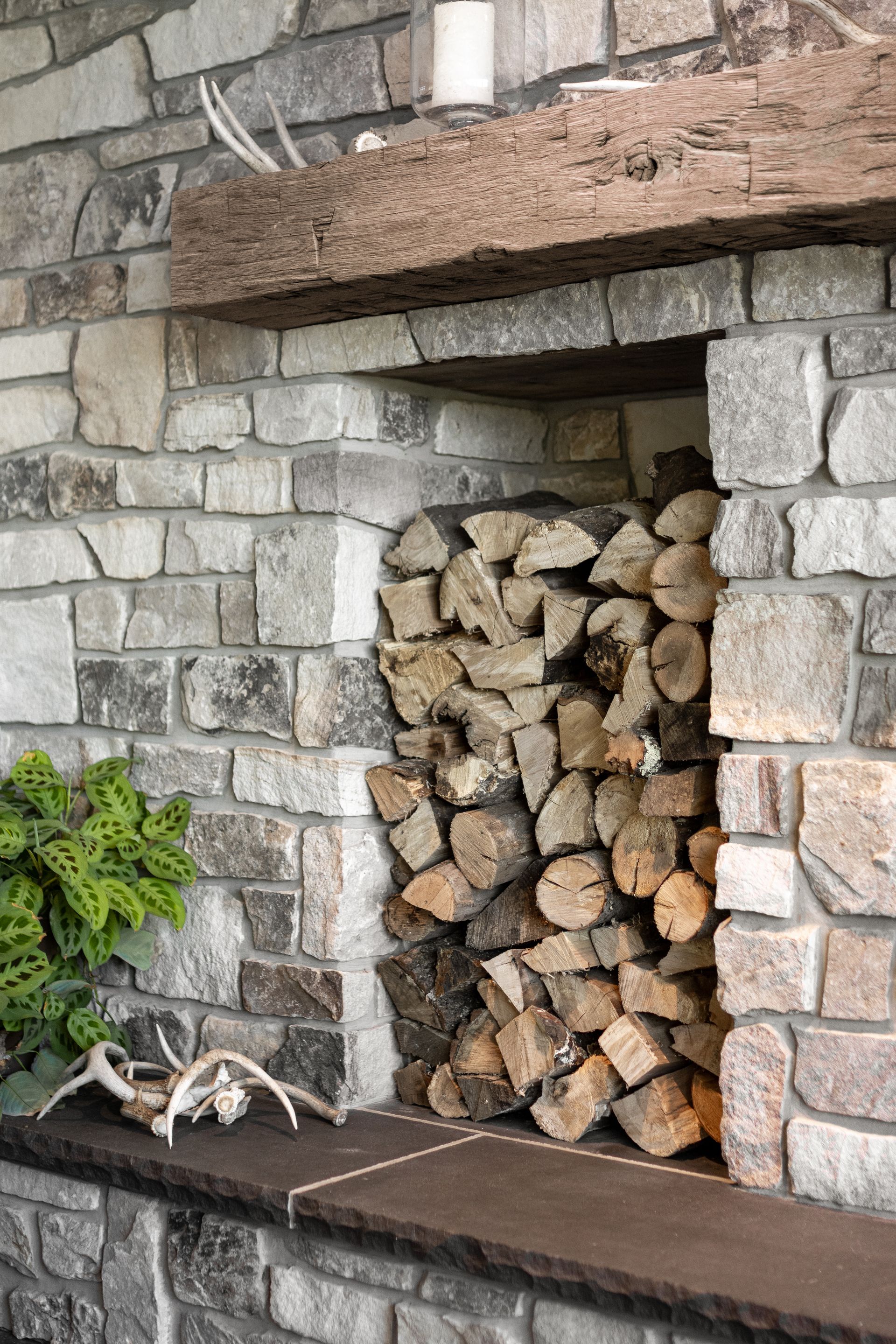 Stone fireplace with stacked firewood in a small outdoor alcove