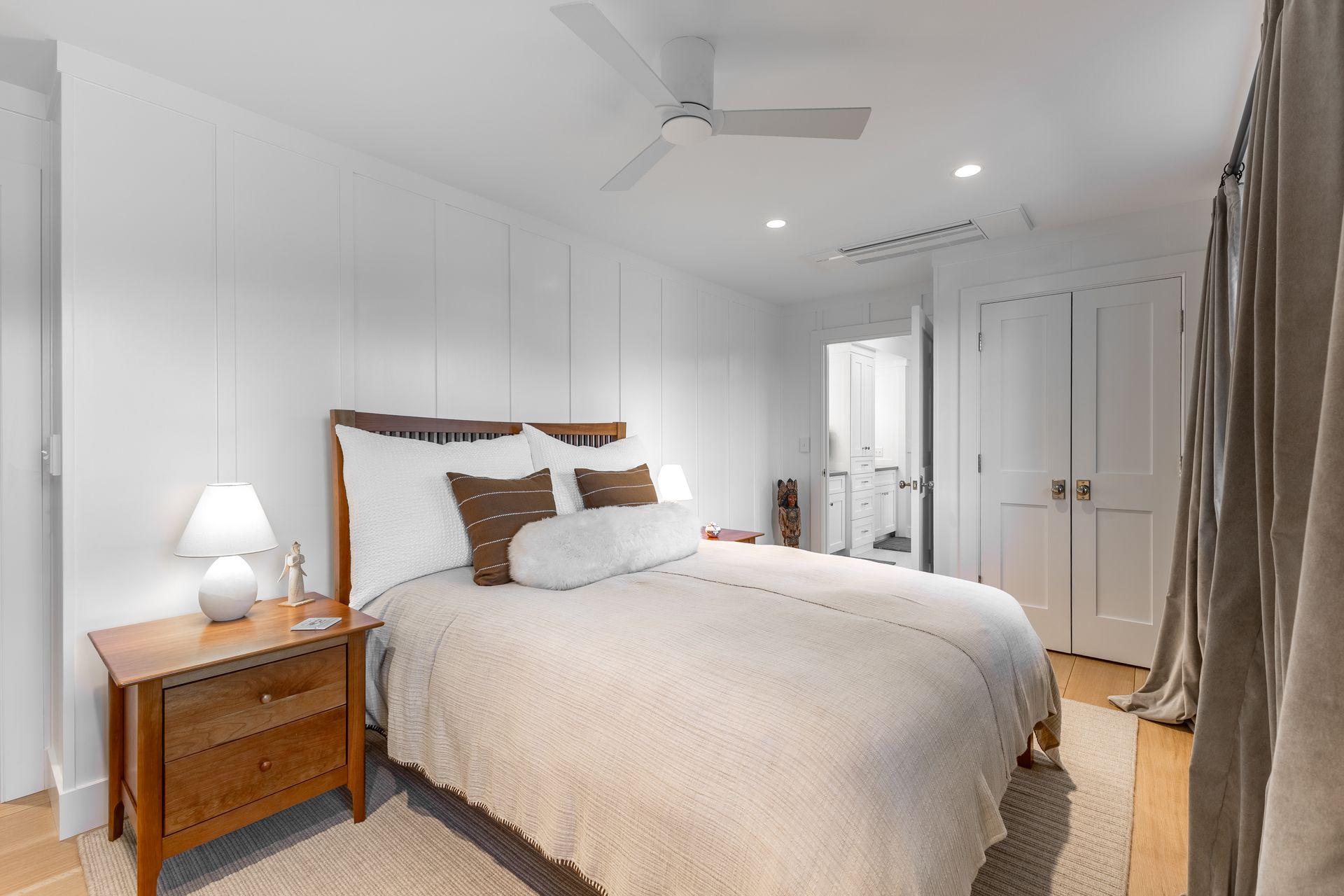 Bright bedroom with a neatly made bed, wooden nightstand, ceiling fan, and white closet doors