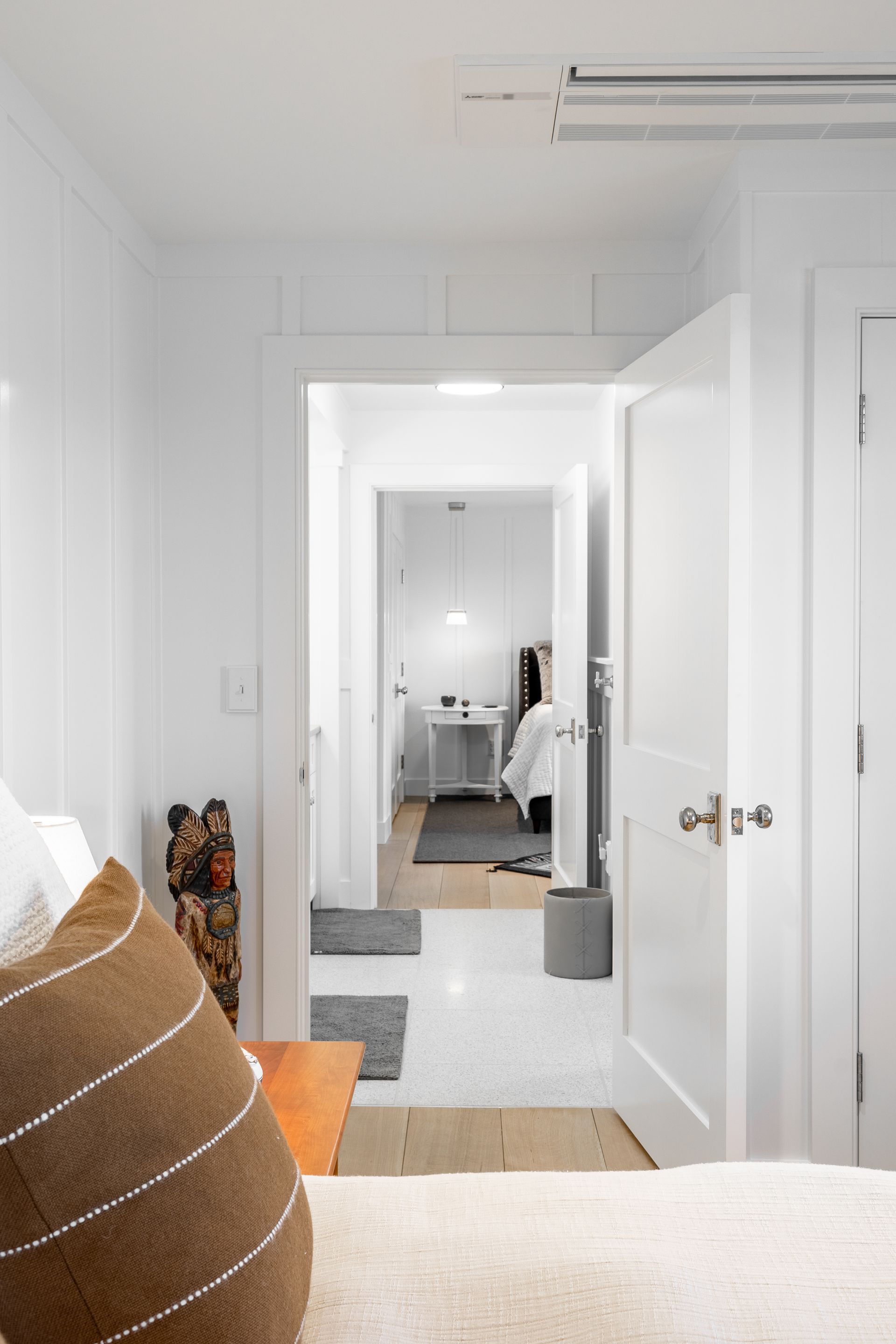 Bright white hallway with open doors leading to a bedroom and desk area, viewed from a bed.