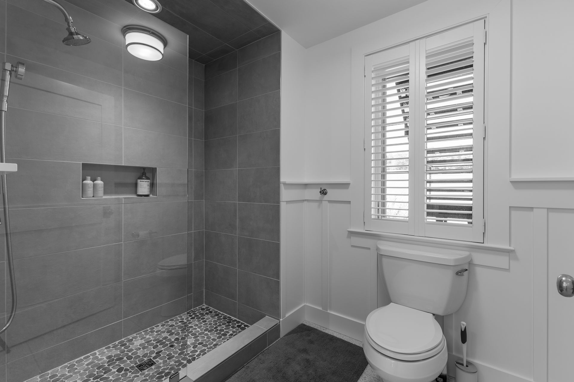 Modern bathroom with tiled shower, toilet, and window with blinds