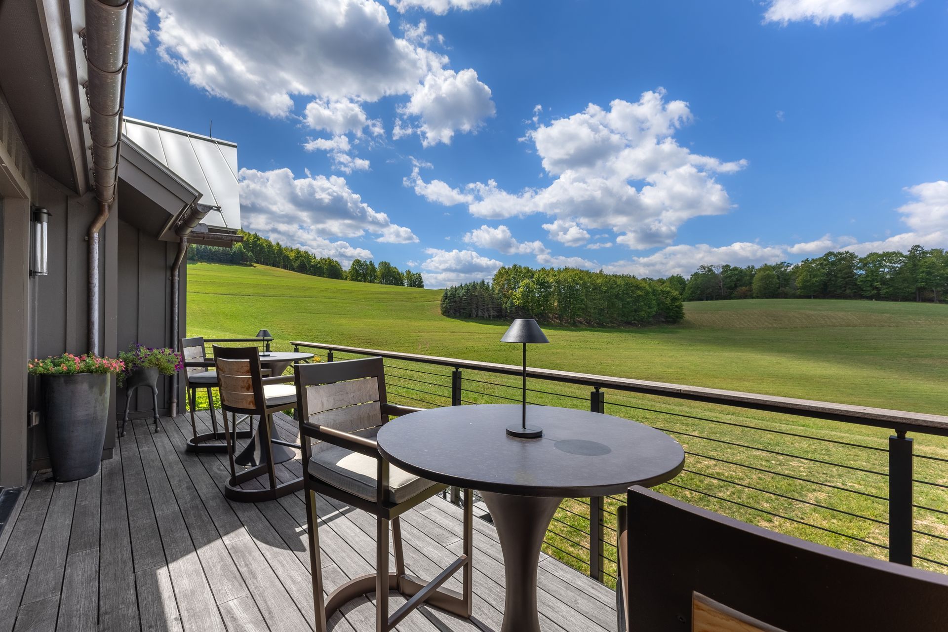 Patio tables overlooking a green field under a bright blue sky with scattered clouds