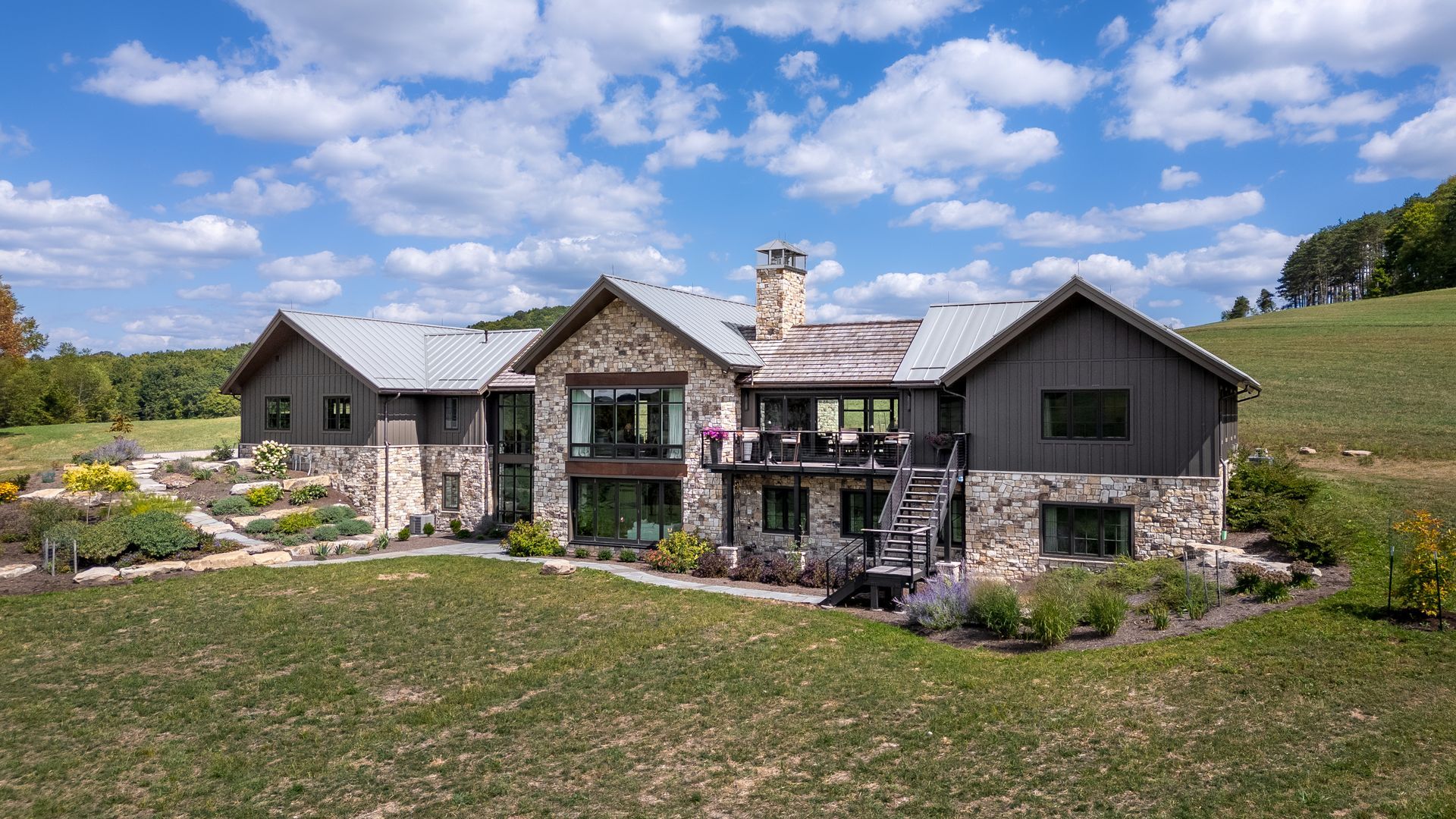 Stone ranch house with a central chimney and large windows, set in a grassy field under a blue sky.