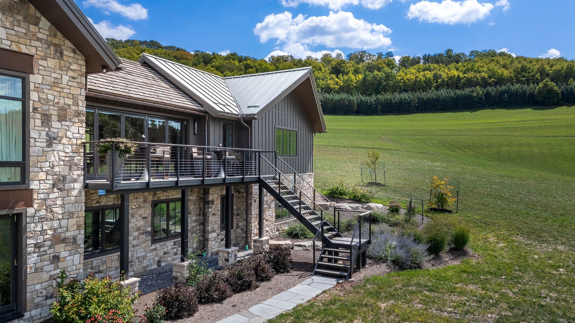 Stone house with balcony overlooking a green field and wooded hillside under a blue sky