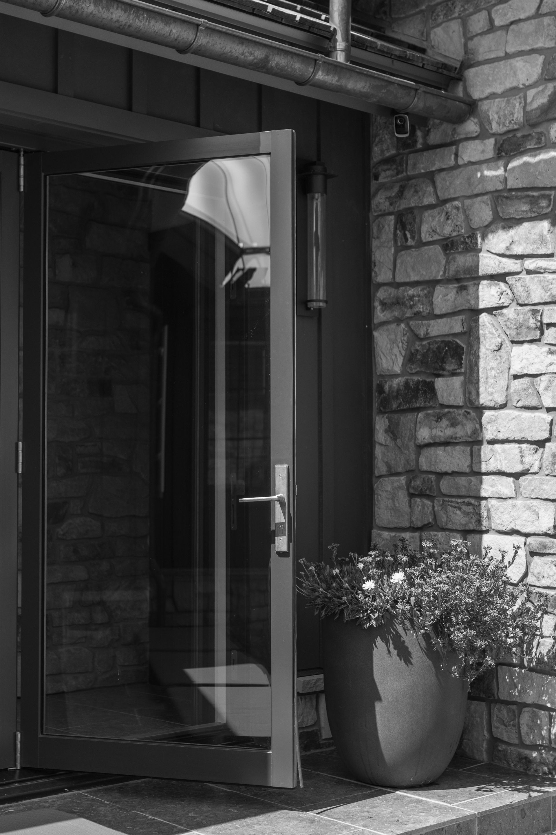 Open glass door at a brick building entrance with a potted plant nearby.