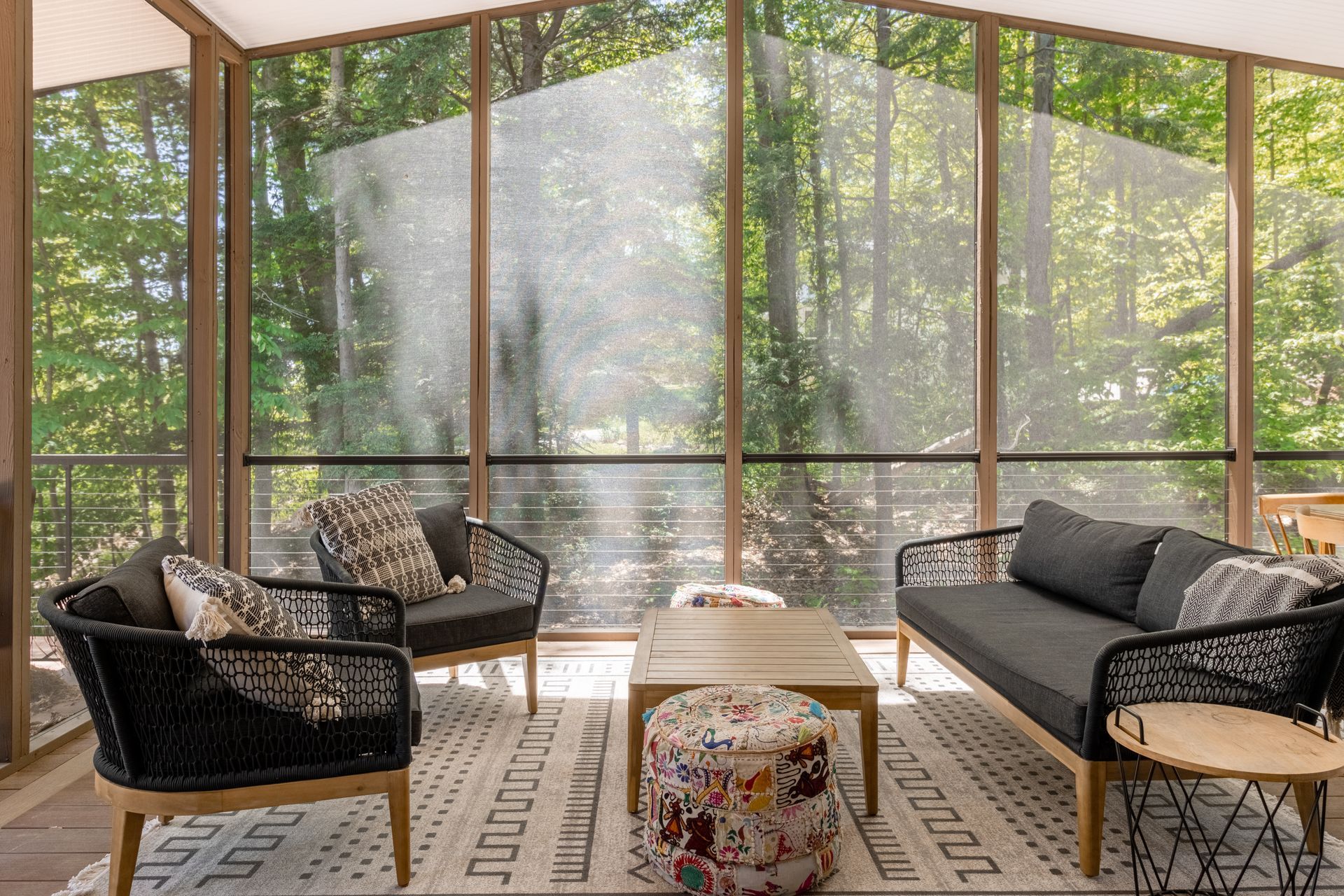 Screened sunroom with wicker seating, patterned rug, and small table overlooking greenery.