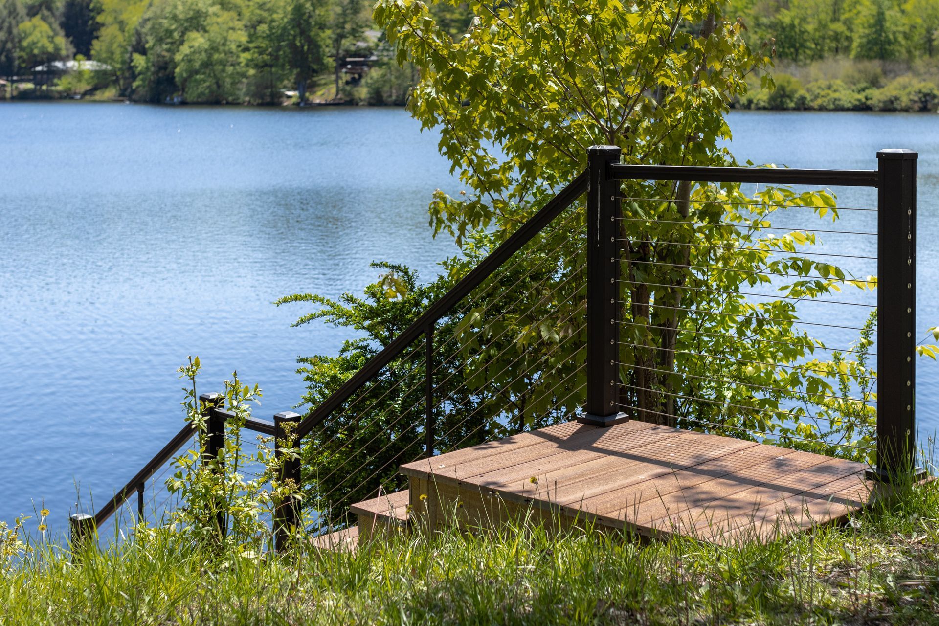 Small dock steps by a calm lake with a black railing and green trees