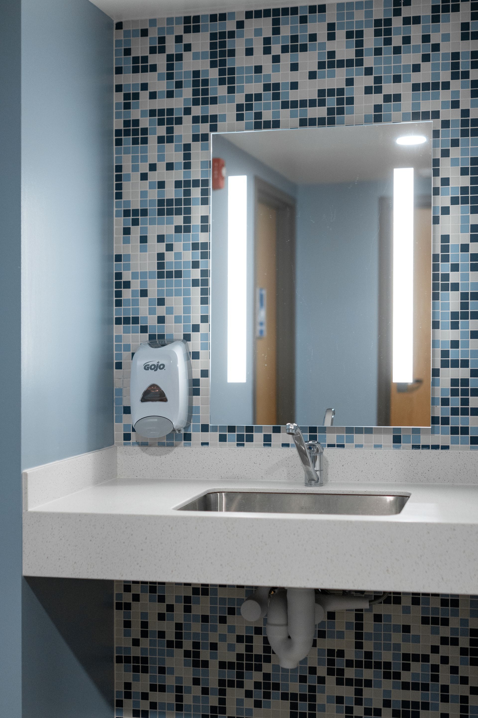 Hamilton Hall bathroom sink with mirror, blue mosaic tile backsplash, and soap dispenser overhead