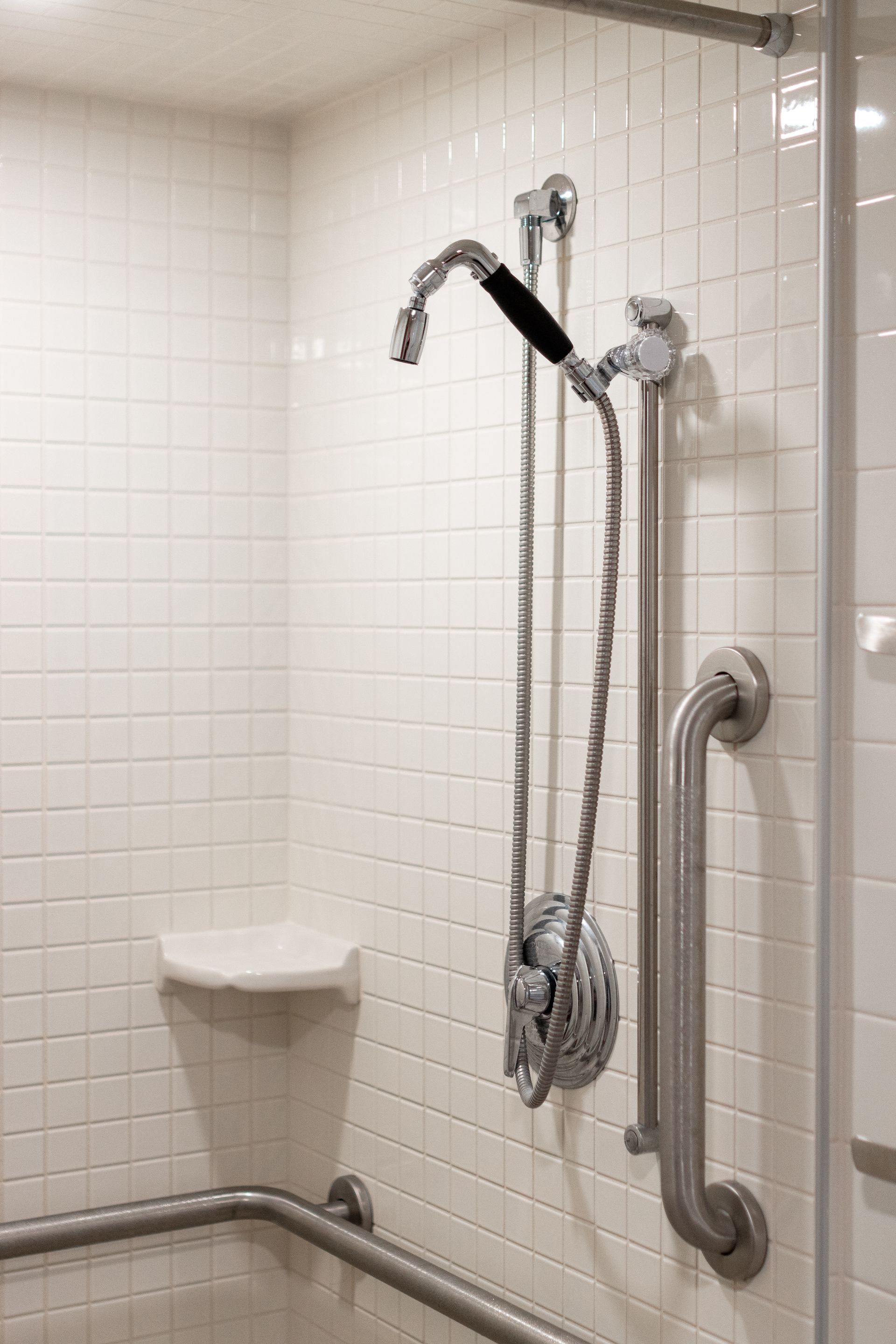 Hamilton Hall accessible bathroom shower stall with a handheld showerhead, grab bars, and built-in seat in a tiled bathroom.
