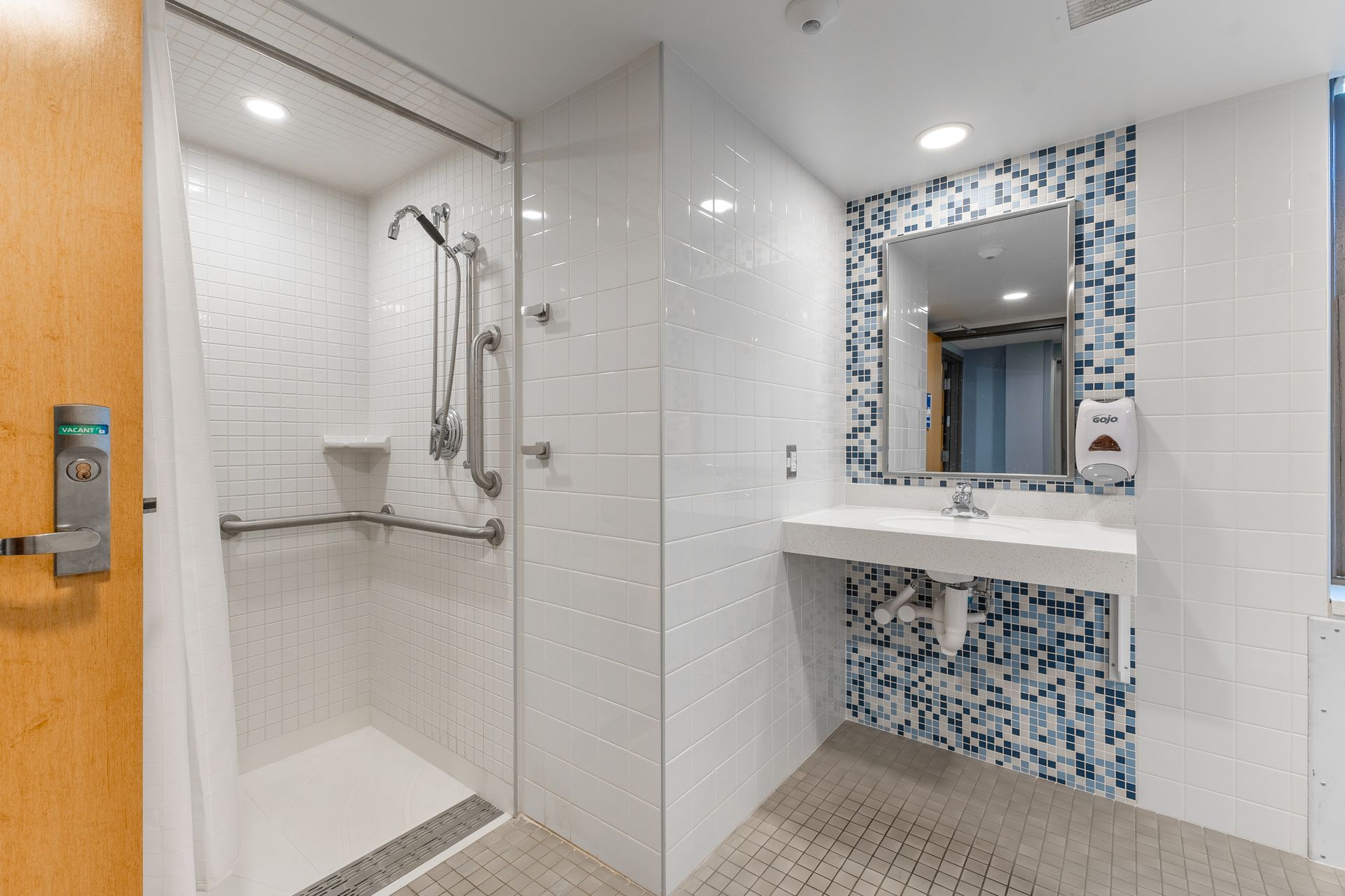 Hamilton Hall bathroom with glass shower, vanity mirror, and blue mosaic accent wall