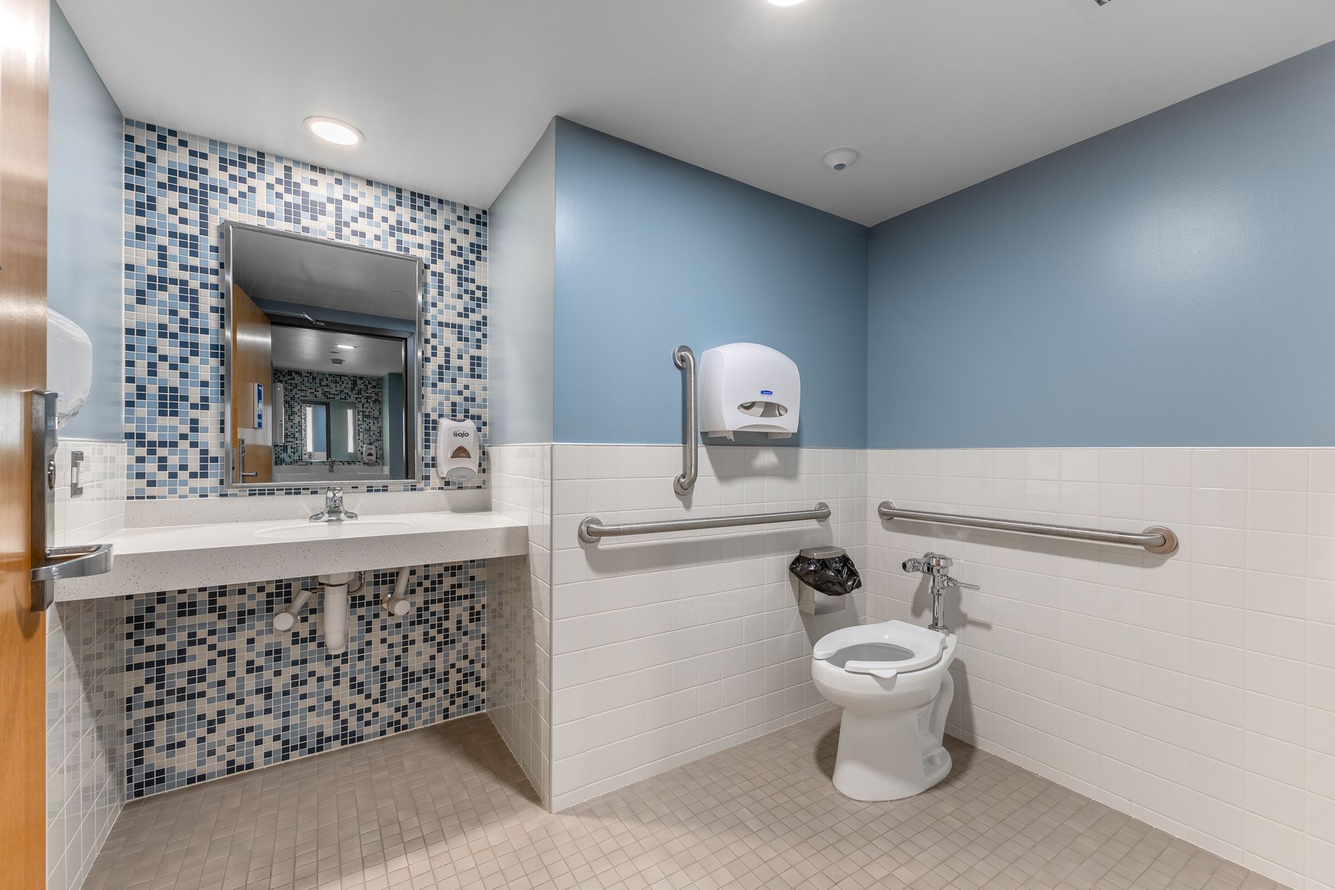Hamilton Hall accessible bathroom with blue walls, grab bars, toilet, sink, and mosaic-framed mirror