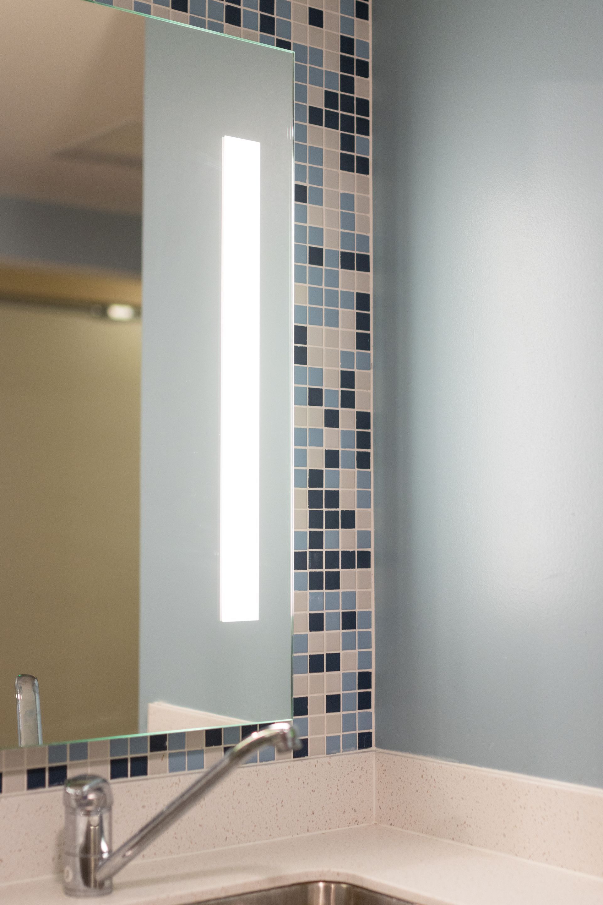 Hamilton Hall bathroom's sink and mirror with mosaic tile border and vertical light strip.