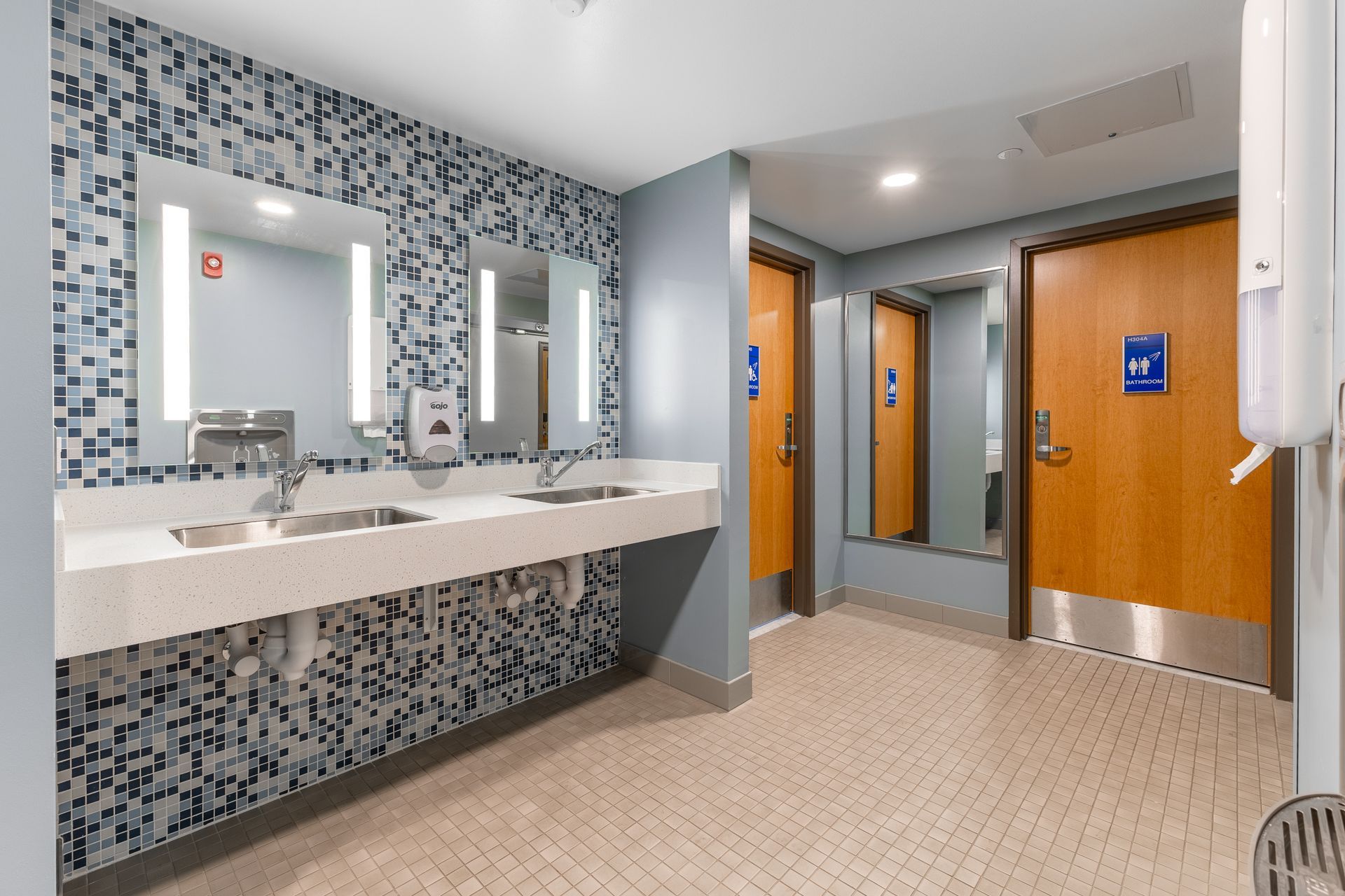 Hamilton Hall bathroom with patterned tile, double sinks, mirrors, and wood stall doors