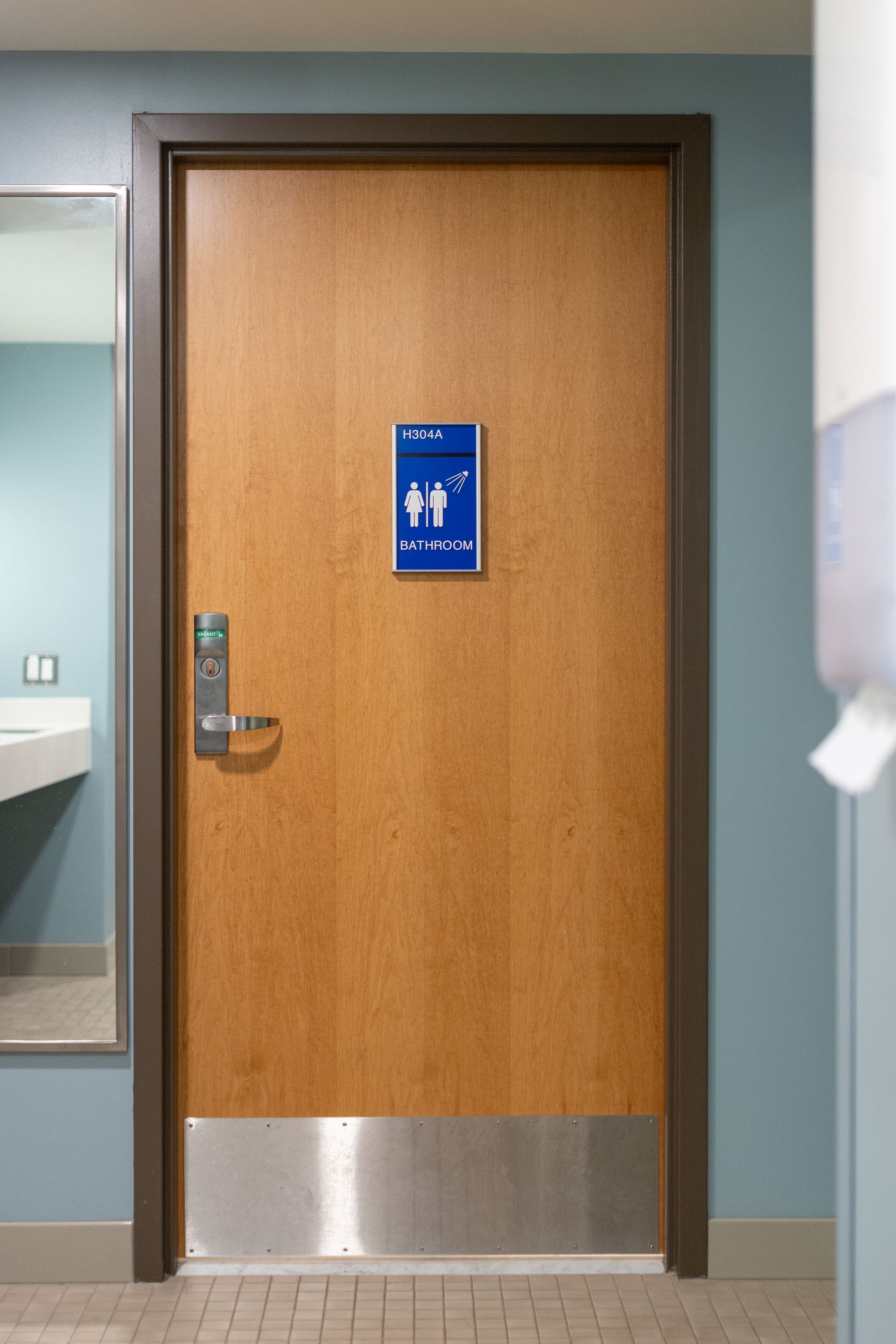 Hamilton Hall bathroom's door with blue accessibility sign and metal push plate in a hallway