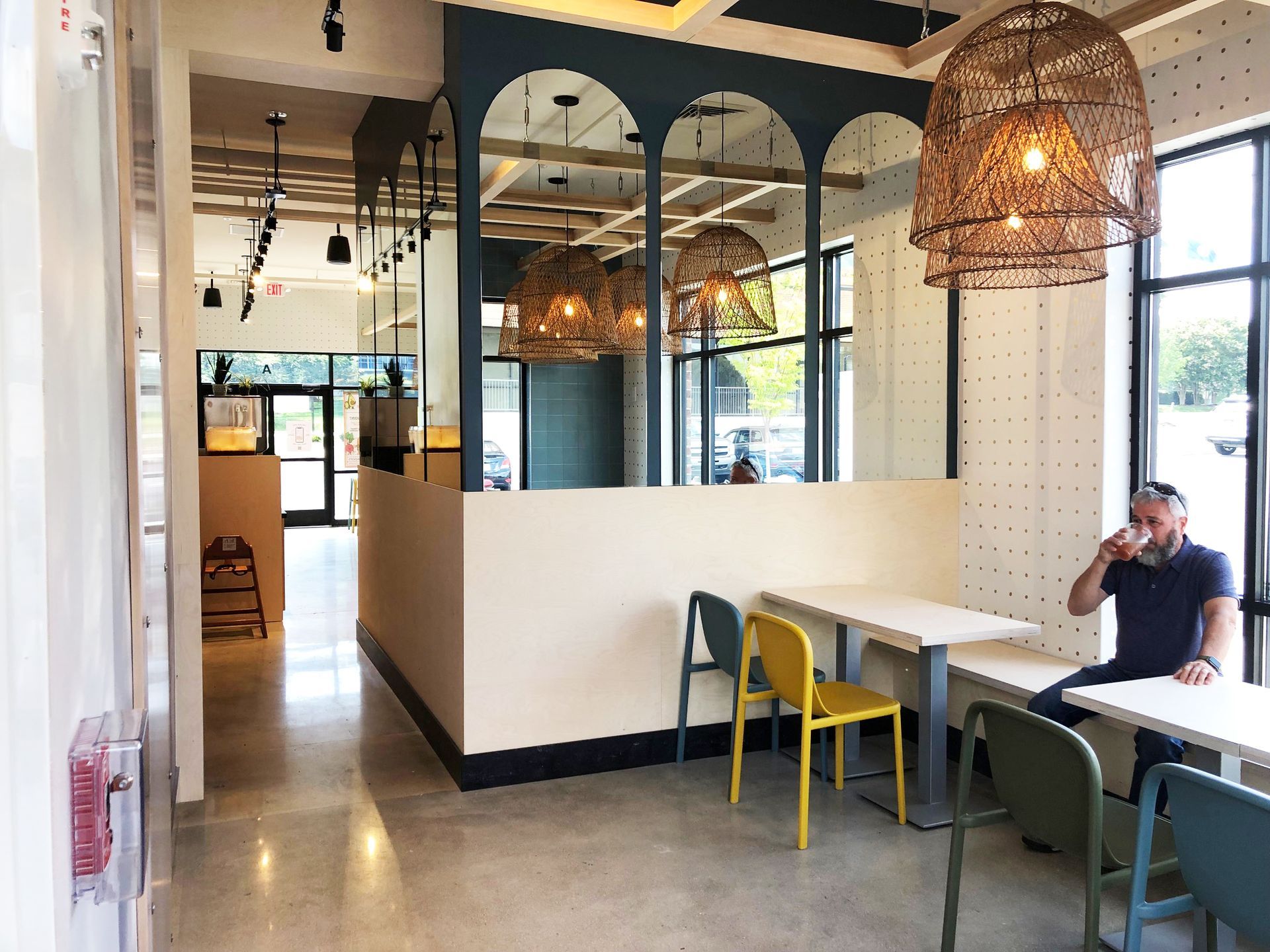 Roots Natural Kitchen interior with white tables, colorful chairs, woven pendant lights, and a person sitting by the window