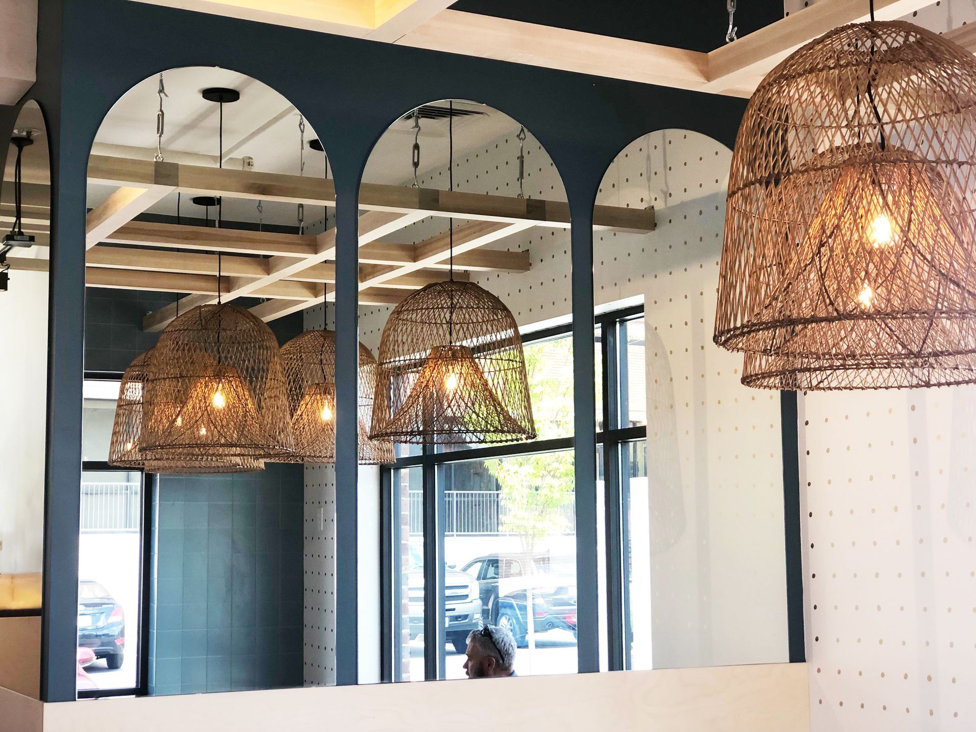 Woven pendant lamps glowing under arched mirrors in Roots Natural Kitchen