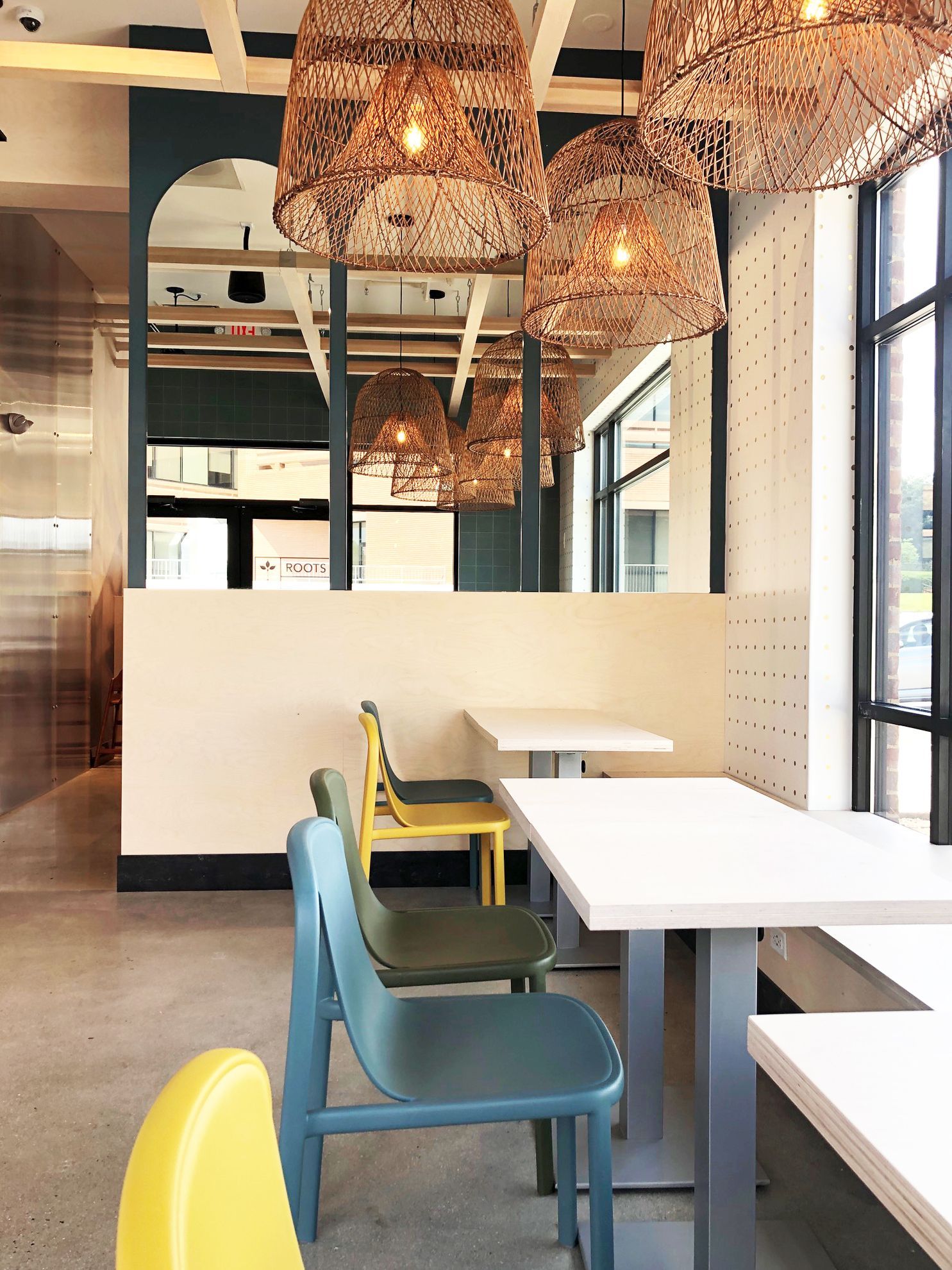 Roots Natural Kitchen interior with blue and yellow chairs, white tables, and woven pendant lights