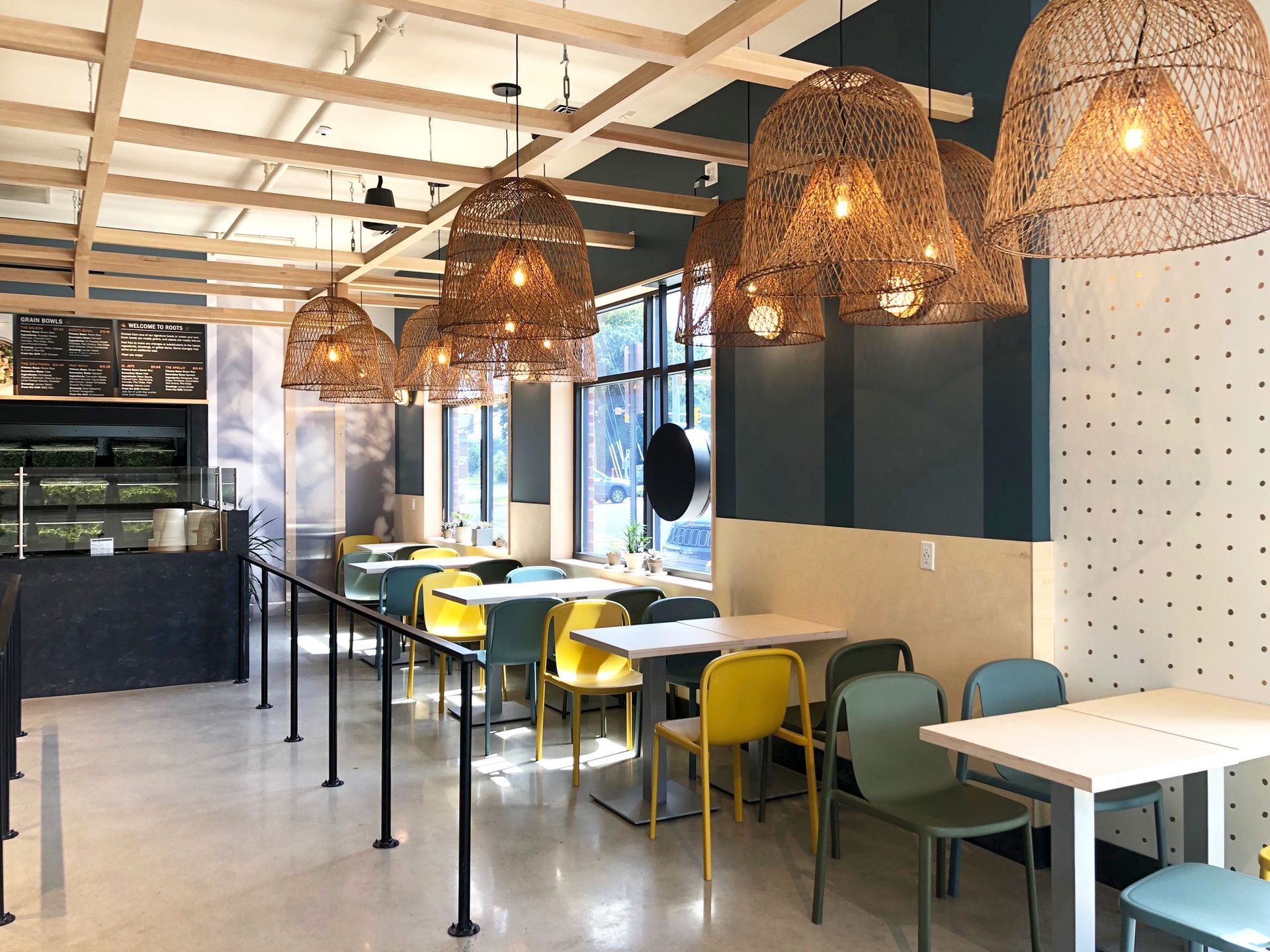 Roots Natural Kitchen interior with wicker pendant lights, yellow chairs, and tables along a windowed seating area
