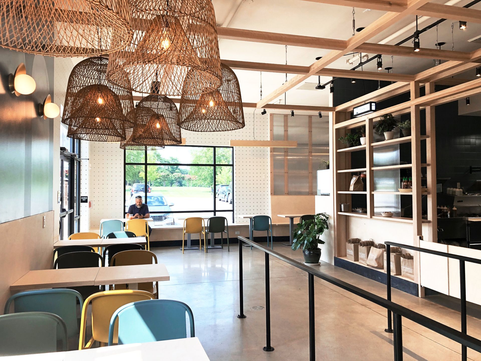 Roots Natural Kitchen interior with hanging lights, tables, chairs, and a person seated by a window