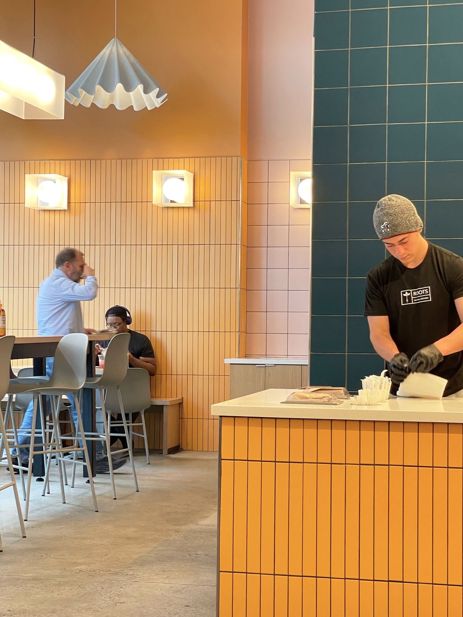 Cafe interior: barista preparing food at counter, customers seated at tables.