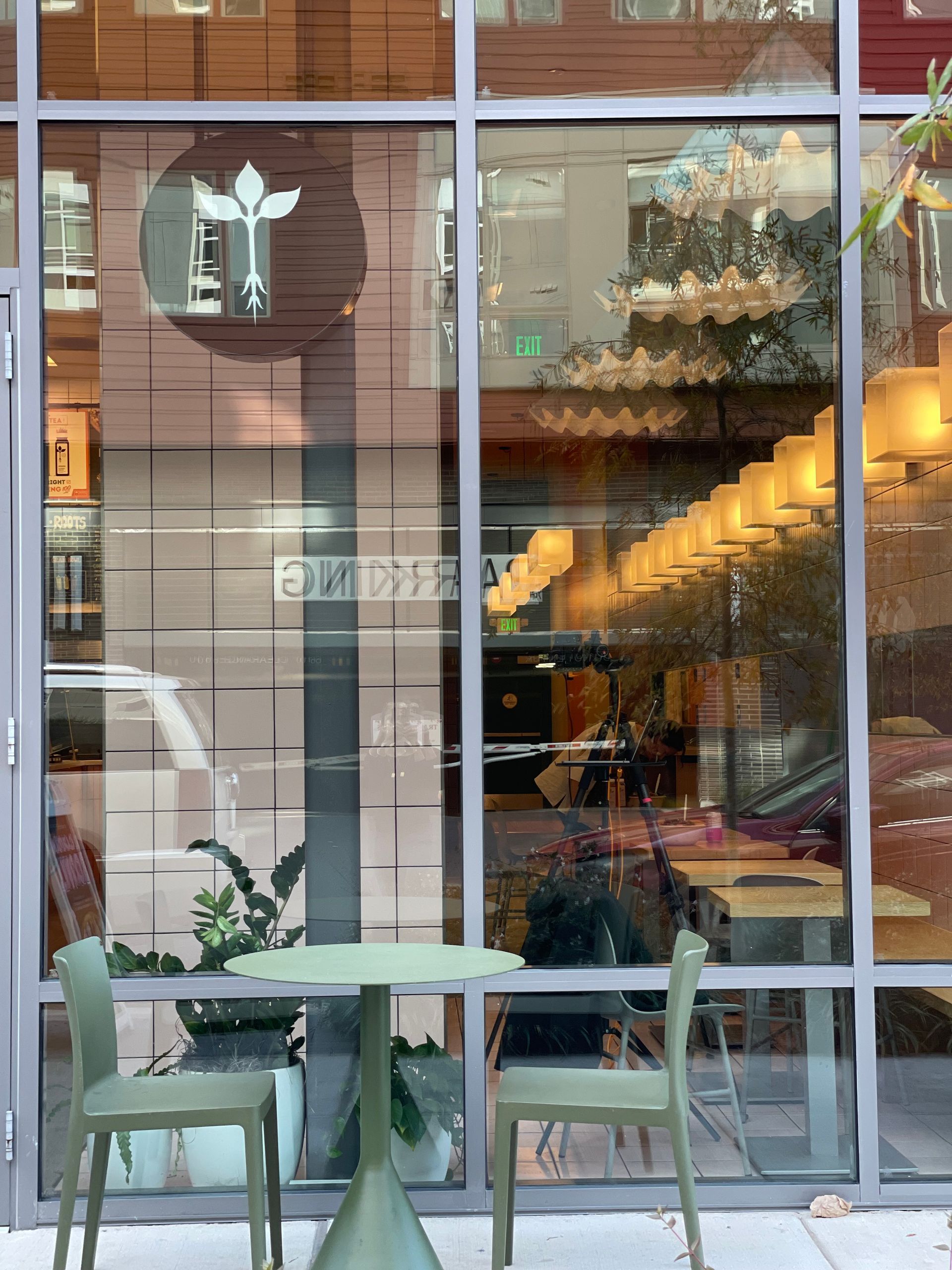 Outdoor seating at a restaurant with large windows; green chairs and table in front of glass.