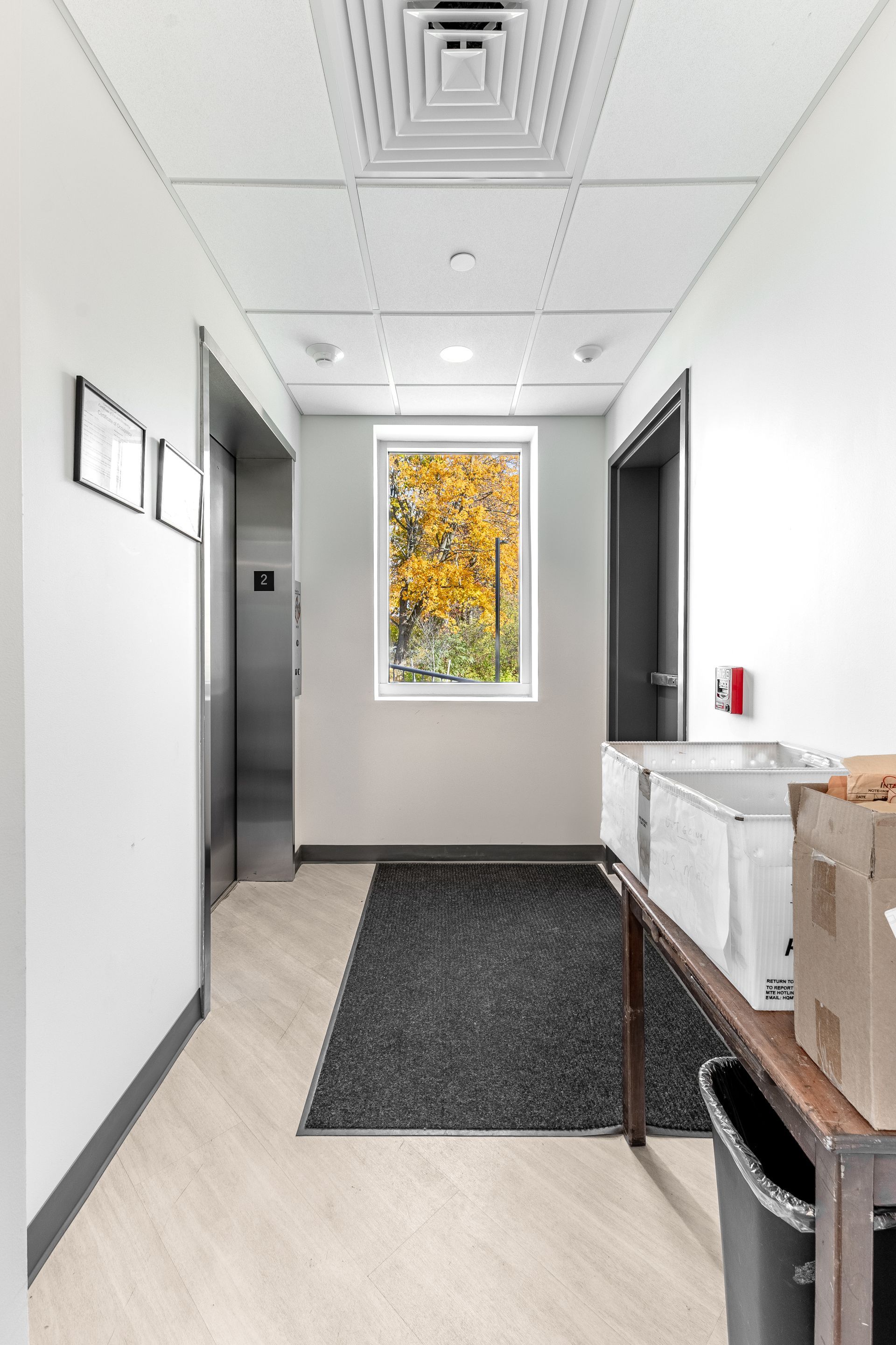 State College Area School District Physical Plant Building's hallway with open doors, black rug, and a colorful window at the end.