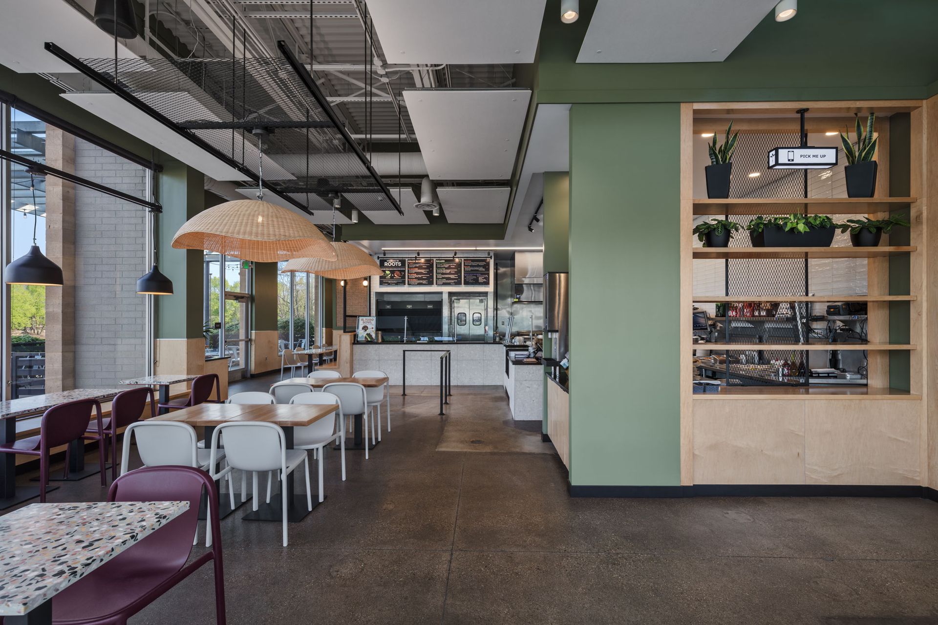 Roots Natural Kitchen's interior with tables, chairs, pendant lights, and a green accent wall with shelving.