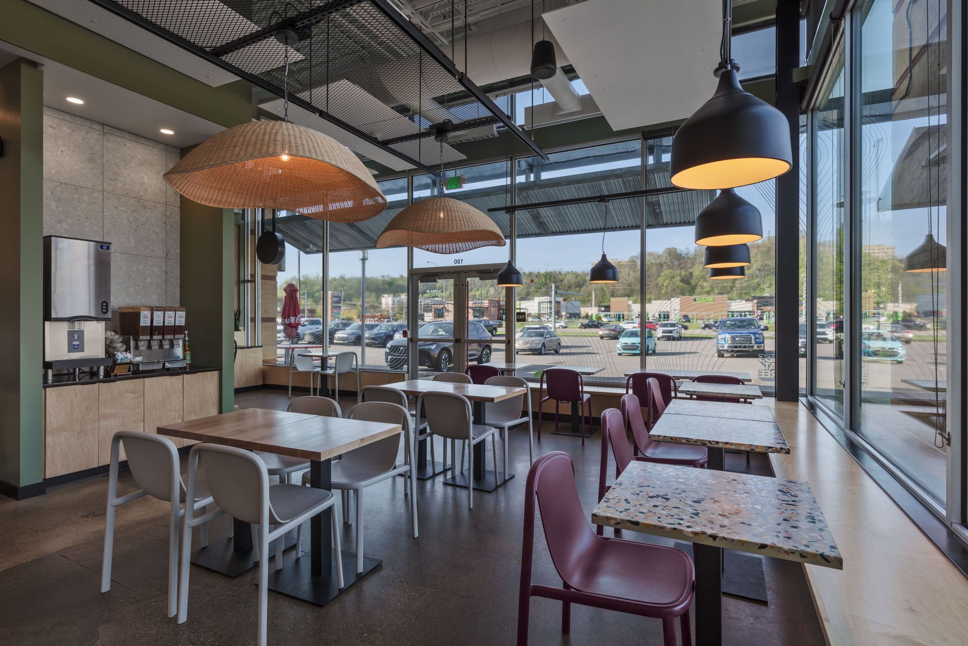 Roots Natural Kitchen's interior with tables, chairs, hanging lamps, and large windows overlooking a parking lot