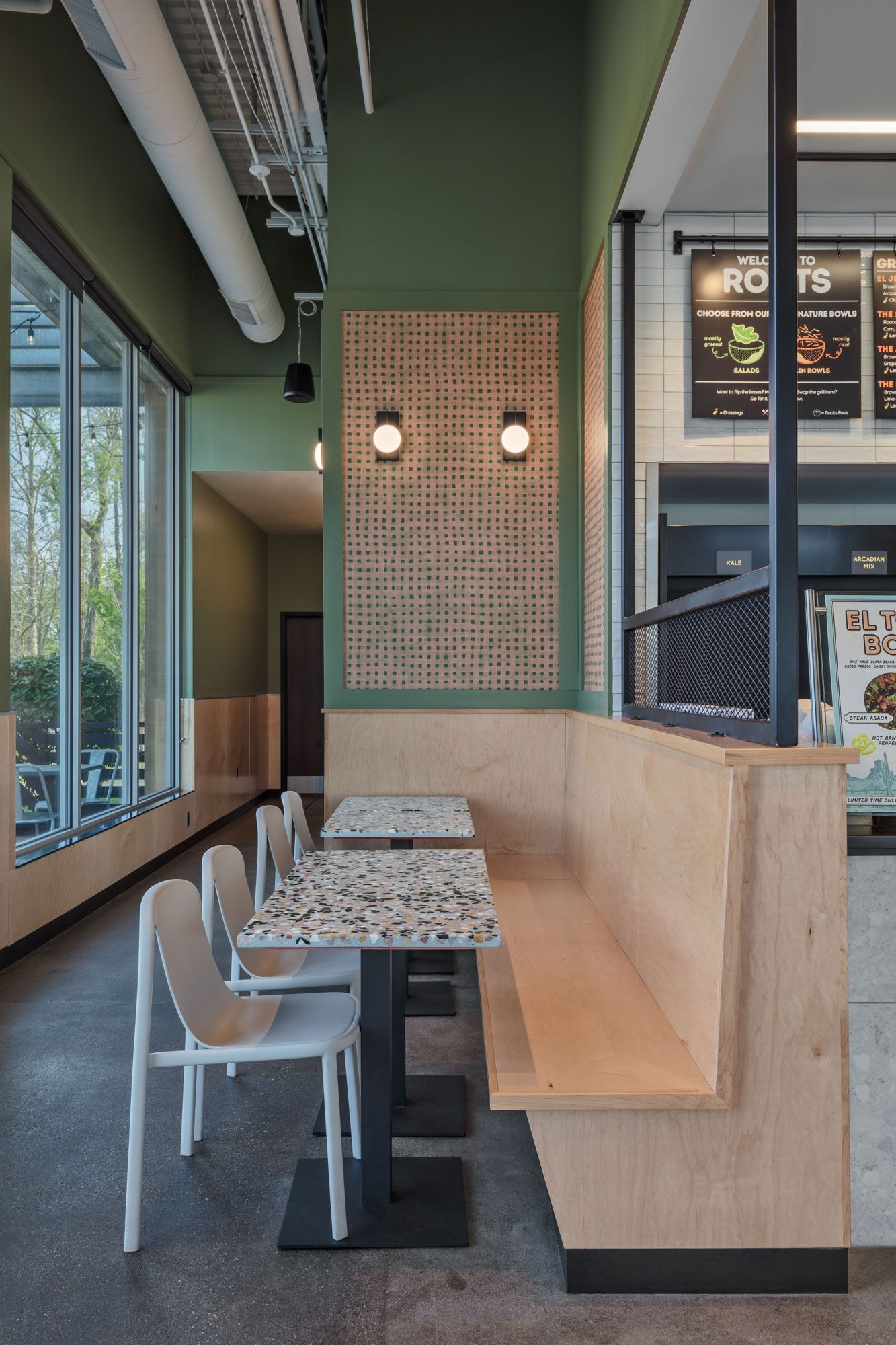Roots Natural Kitchen's interior seating area with marble tables, gray chairs, green wall, and large windows