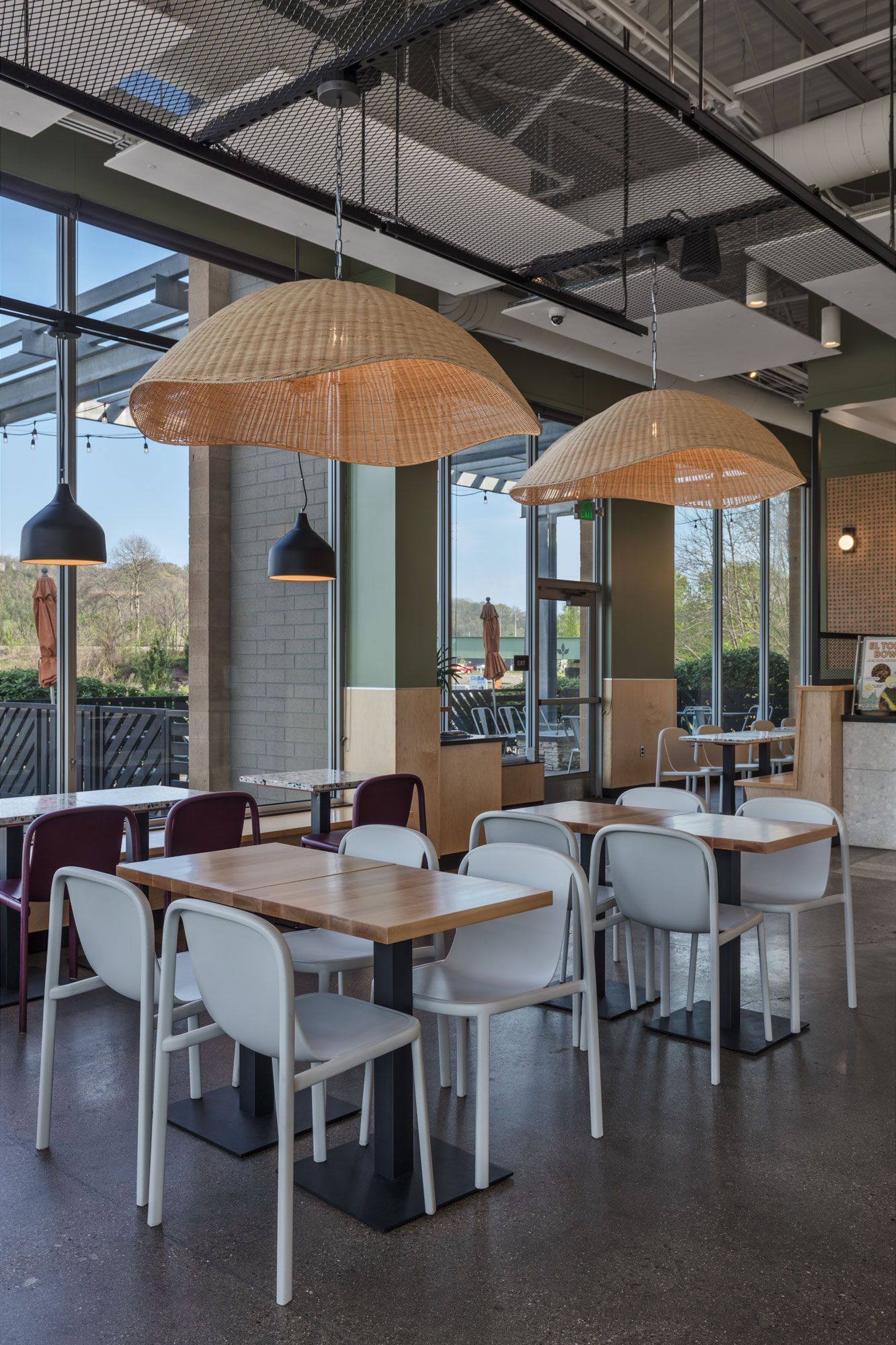 Roots Natural Kitchen's interior with white chairs, wooden tables, woven pendant lights, and large windows
