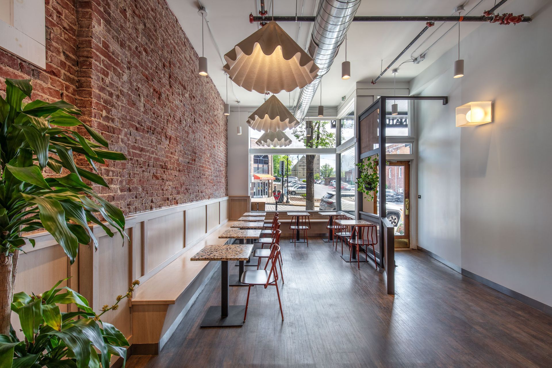 Roots Natural Kitchen's interior with brick wall, wooden tables, hanging lights, and large windows