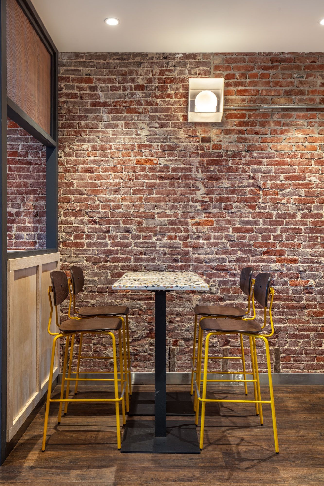 Roots Natural Kitchen's interior table with two yellow chairs against a red brick wall.