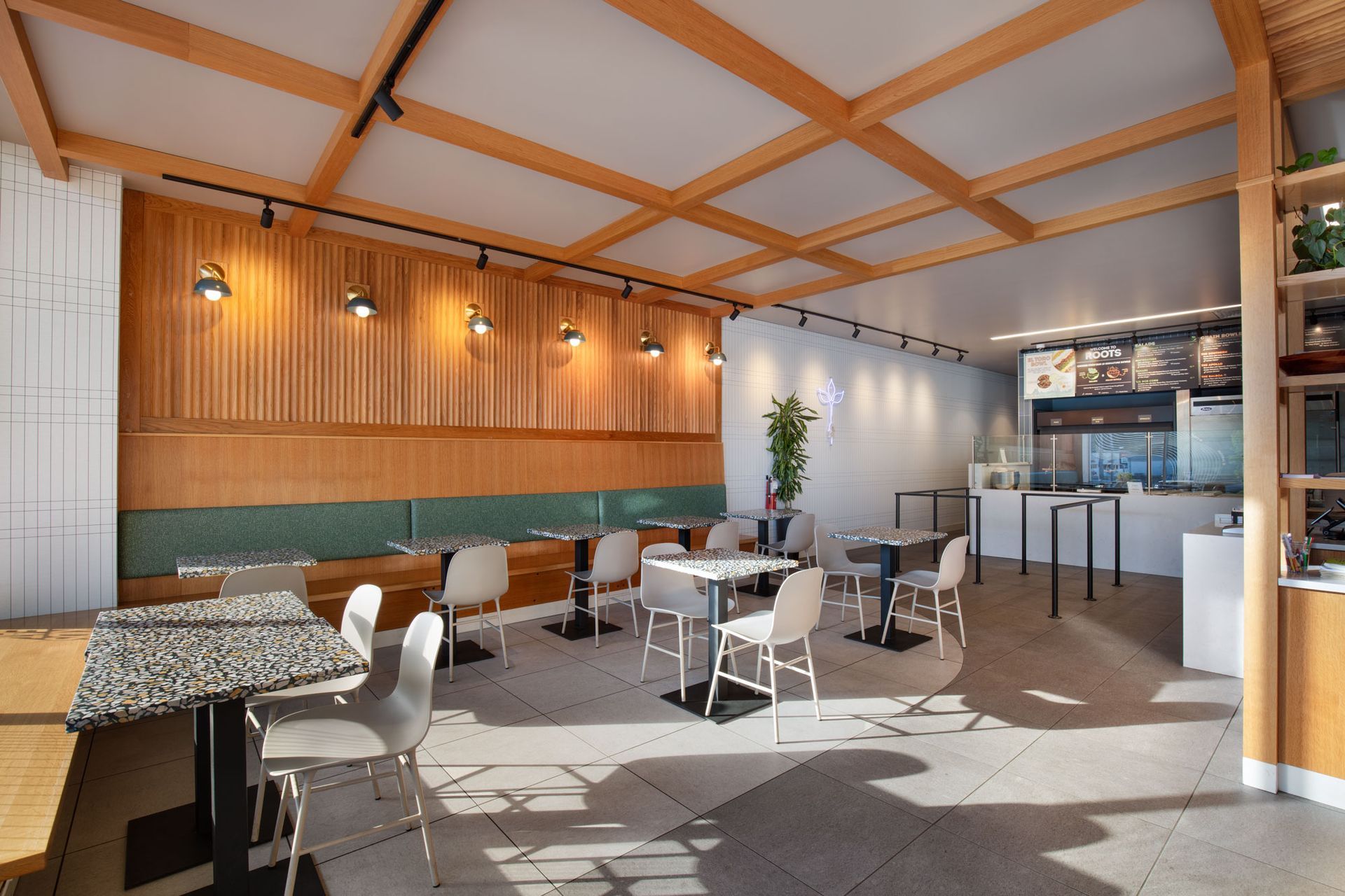 Roots Natural Kitchen's interior with wooden ceiling beams, white chairs, patterned tables, and a bright open seating area