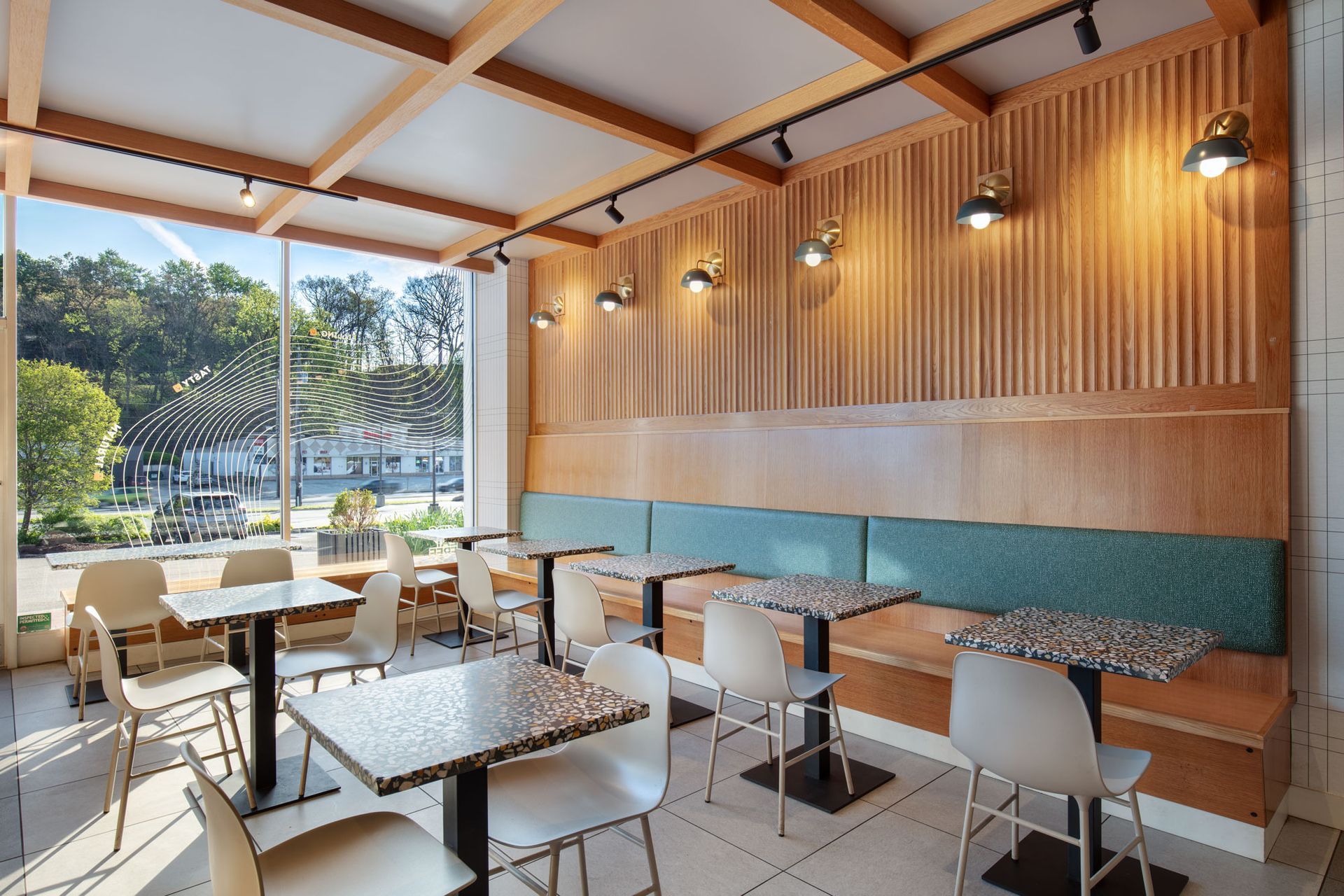 Roots Natural Kitchen's interior with wooden walls, white tables, and large windows overlooking greenery