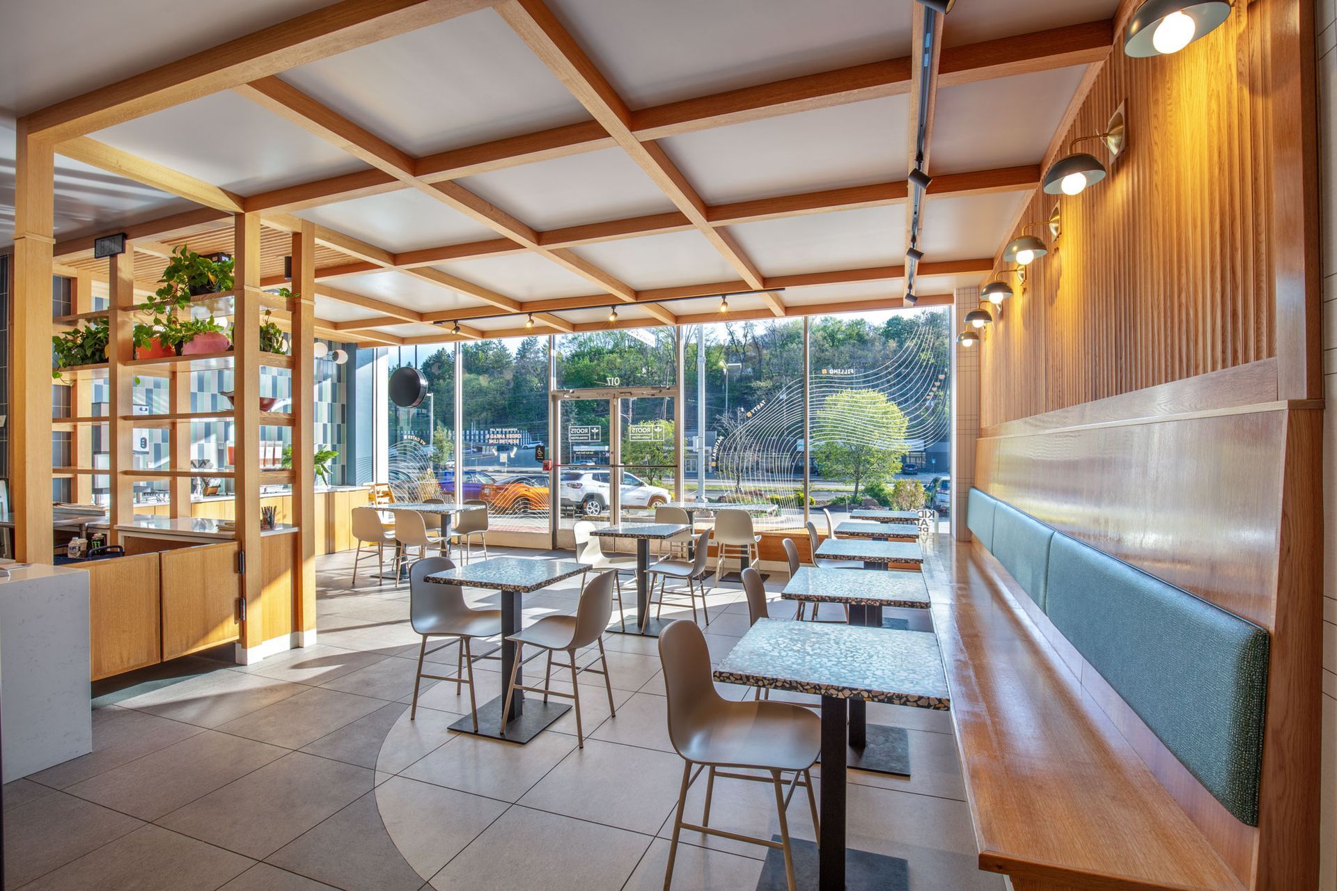 Roots Natural Kitchen's interior with wooden ceiling, white tables, and large windows overlooking greenery